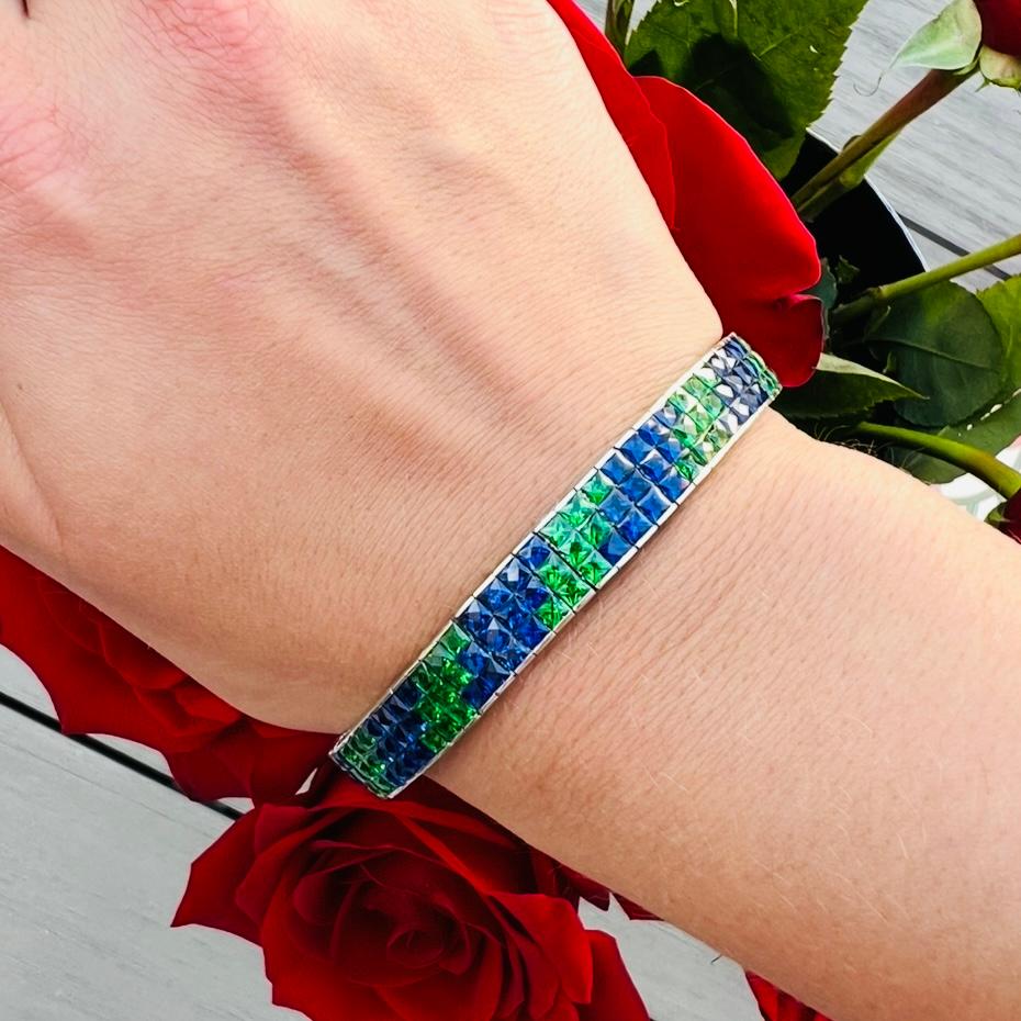 Ce bracelet unique et magnifiquement réalisé, serti de pierres précieuses invisibles, ne manquera pas de plaire ! Le bracelet souple en or blanc 18k est conçu avec 198 saphirs et tsavorites de taille française, pesant au total environ 29,00 carats.