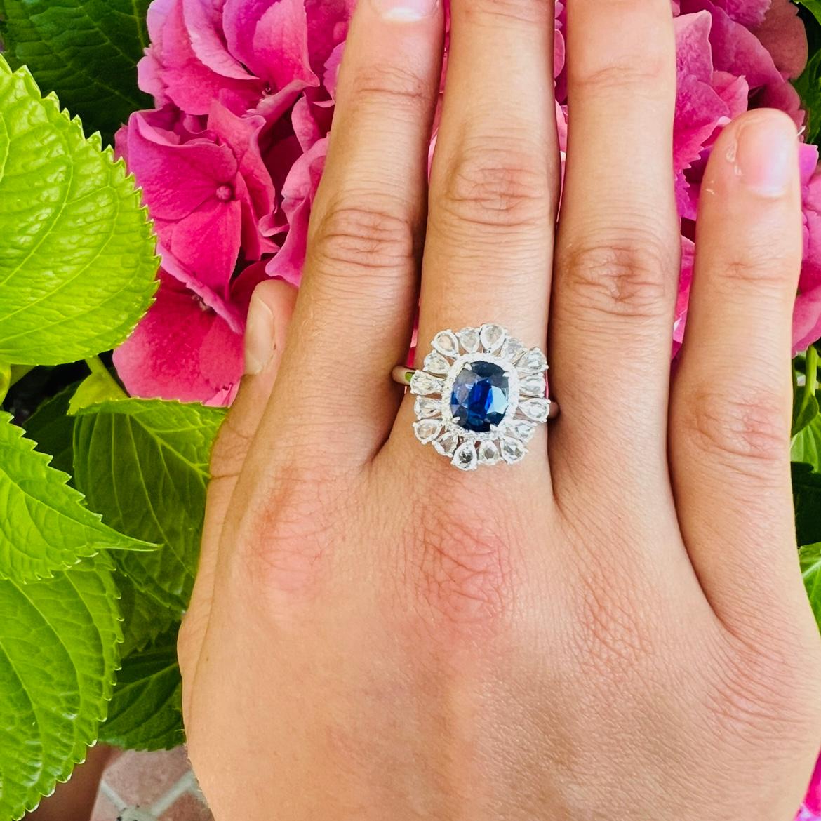 Ein klassisches Design neu interpretiert! Im Mittelpunkt des Platinrings steht ein ovaler, tiefblauer Saphir mit einem Gewicht von 1,23 Karat, der von einem runden Diamanten und einem Kranz aus birnenförmigen weißen Saphiren umgeben ist. Der Ring