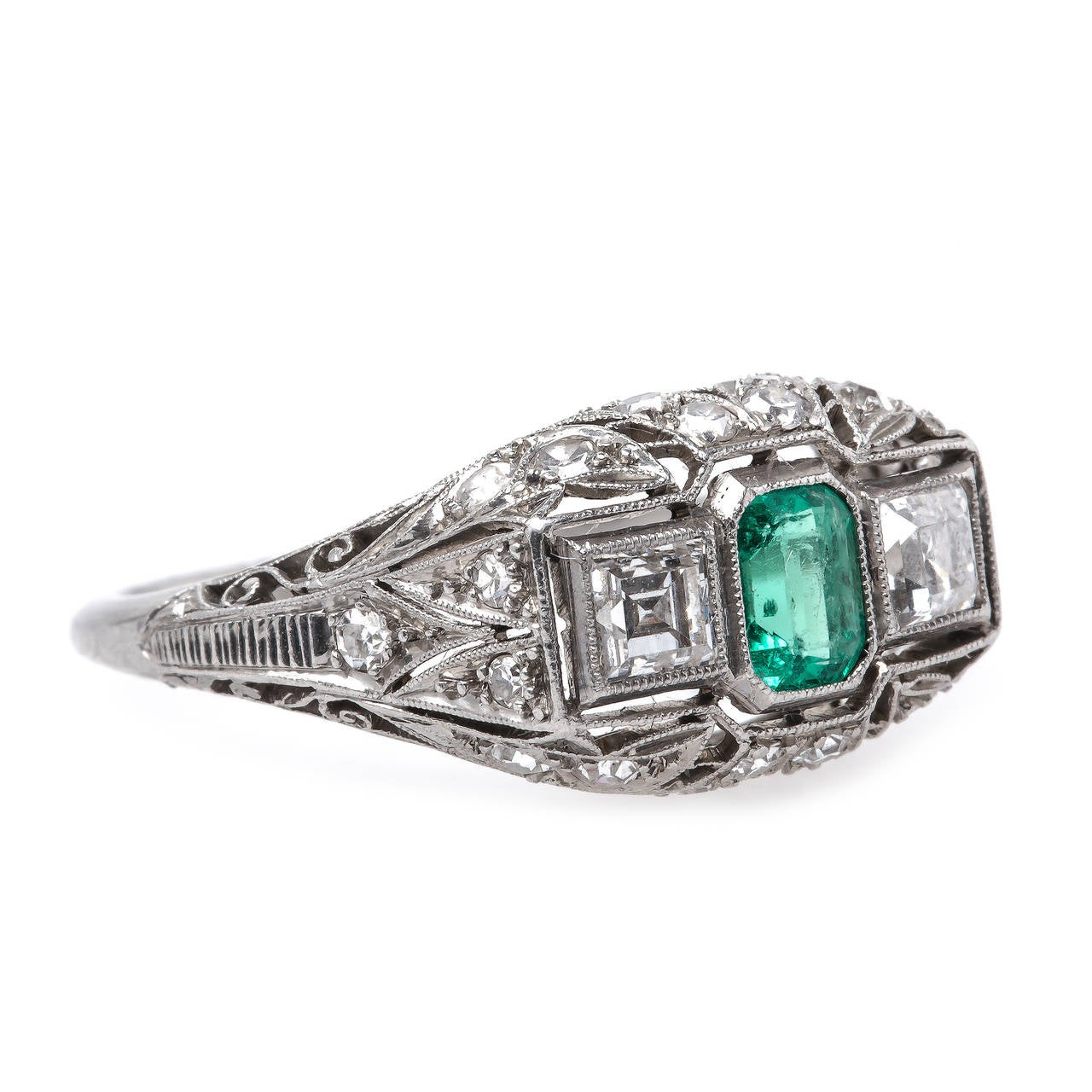 Northbridge is an exceptional example of authentic Edwardian (circa 1915) workmanship.  Made from platinum, this elegant ring centers a bezel set bright green Rectangular Step Cut emerald gauged at 0.45ct flanked by two crisp Square Cut diamonds