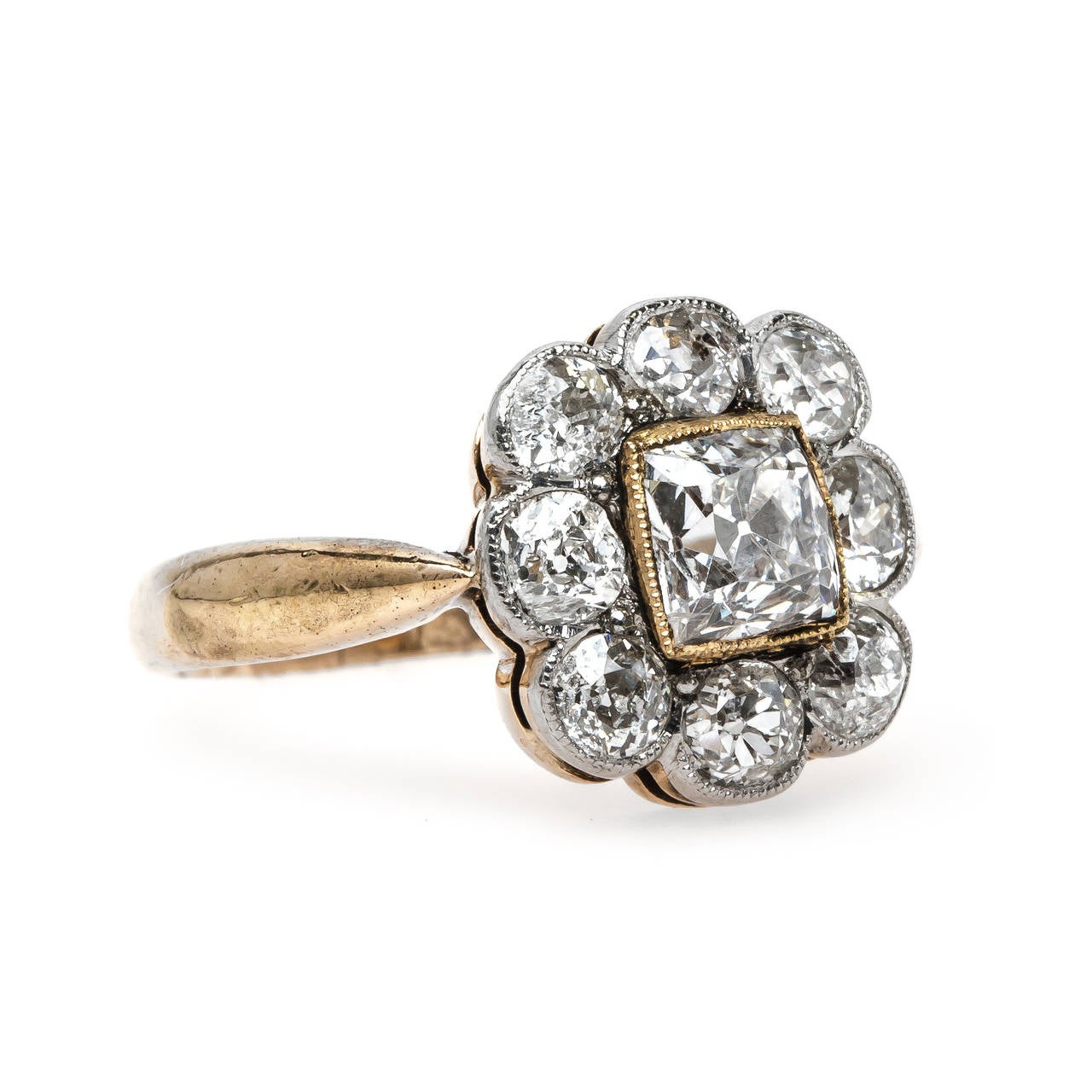 Granada is a wonderfully unique Victorian era (circa 1880) platinum topped 14k yellow gold halo style engagement ring. The ring centers a bezel set 0.72ct  EGL certified Cushion Square Modified Brilliant Cut diamond graded F color and SI2 clarity. A