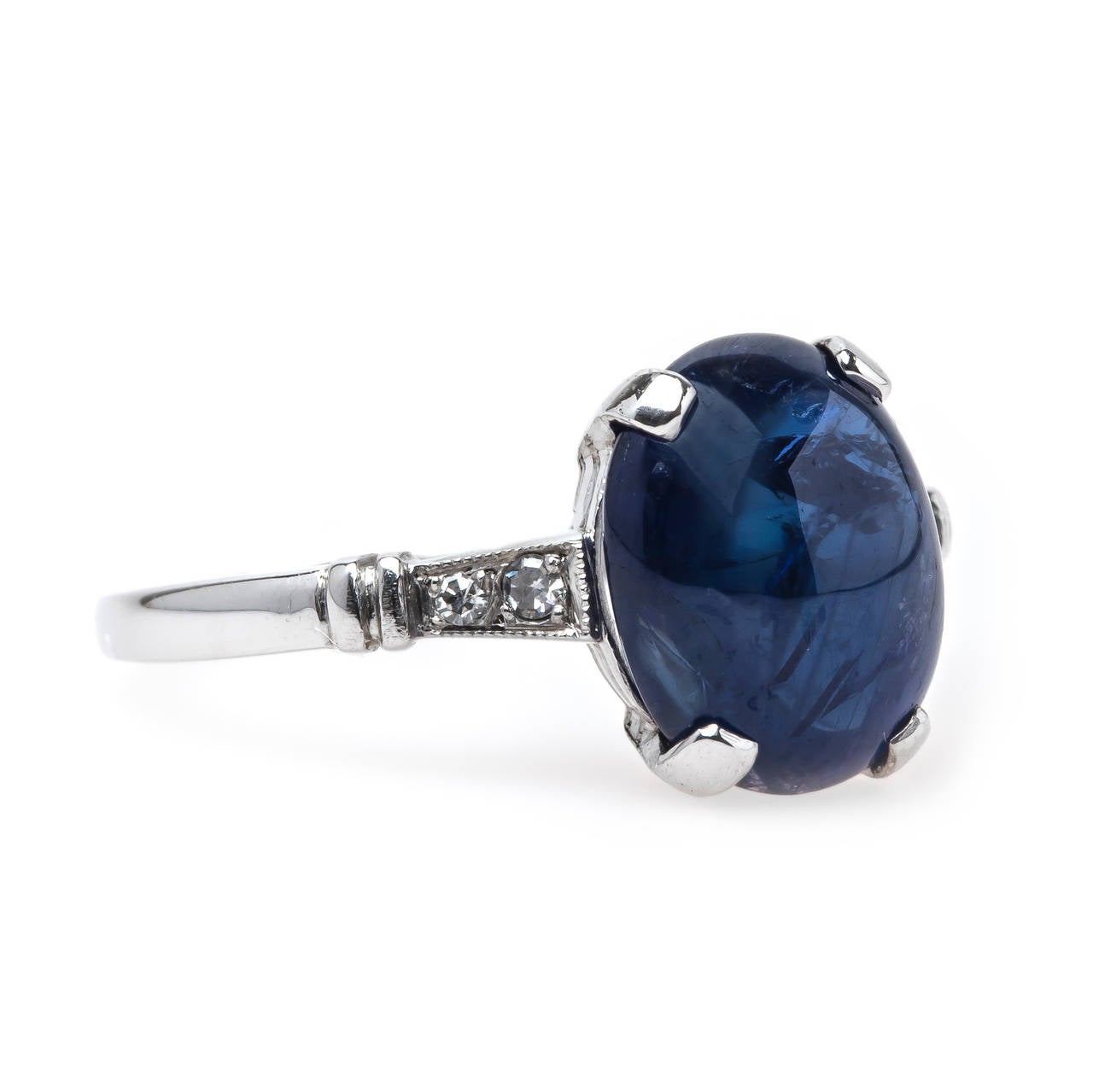 Gulfhaven is a timeless Late Art Deco (circa 1935) ring made from platinum featuring a deep blue natural Oval Cabochon sapphire weighing exactly 4.68cts. This midnight blue sapphire rests in a handmade exemplary Art Deco four-prong setting flanked