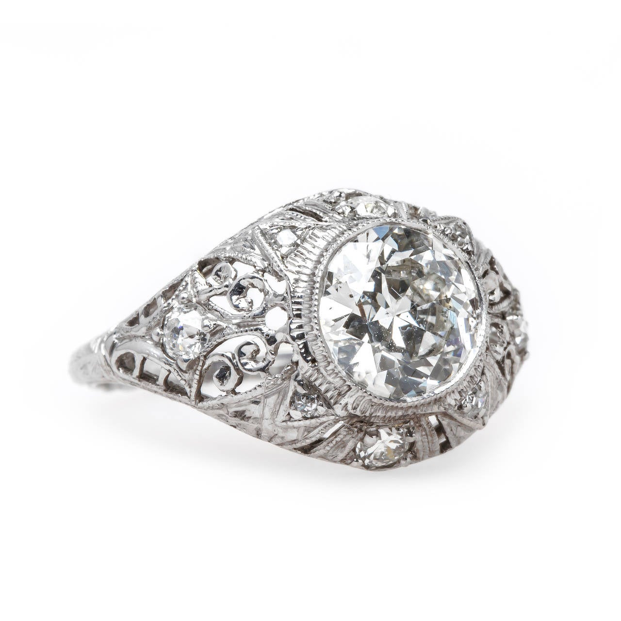 Abernathy is a spectacular Edwardian era (circa 1915) platinum ring centering a bezel set 1.43ct EGL certified Transitional Round Brilliant Cut diamond graded G color and VS2 clarity. The bombe style ring is further adorned with four Old European