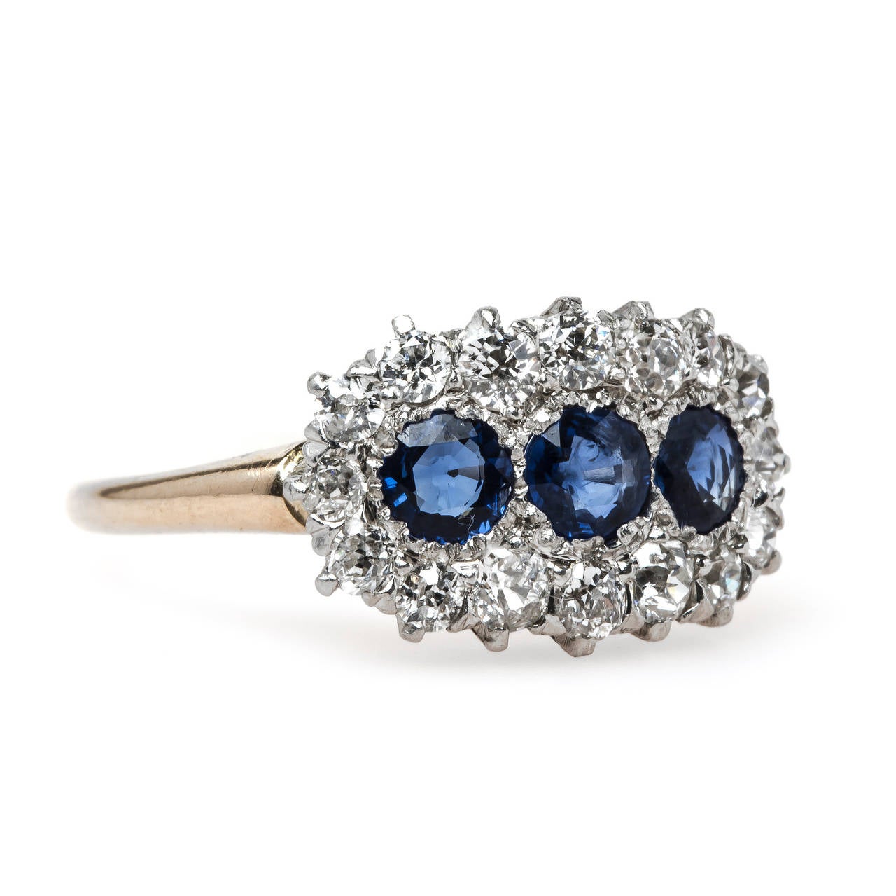 Barbados is a timeless authentic Victorian era (circa 1895) platinum topped 14k yellow gold three stone sapphire halo ring featuring three round natural sky blue sapphires set horizontally gauged at approximately 0.75ct total weight. A shimmering