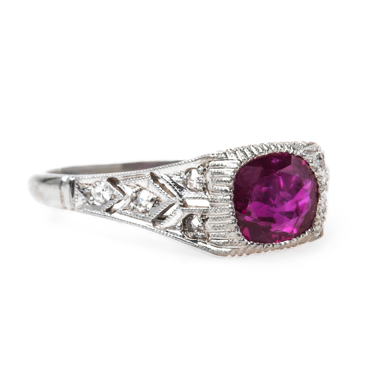 Madeira is a cheerful authentic Art Deco platinum ring centering a ruby weighing exactly 1.31cts accompanied by a Guild Laboratories certificate stating the ruby is heated with a Burma origin. This deep red ruby is bezel set within an angular bombe
