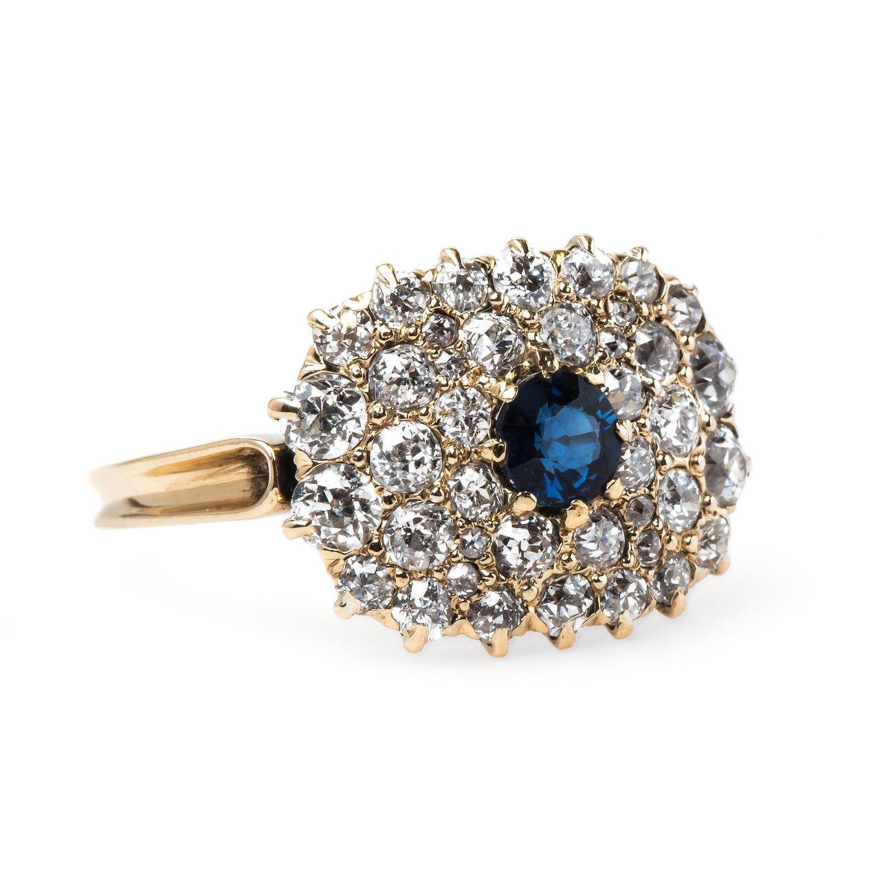 Bunker Hill is a delightful authentic Victorian era (circa 1895) 14k yellow gold sapphire and diamond ring centering a single round natural deep blue sapphire totaling approximately 0.40ct and framed by a cushion shaped cluster of forty-one Old Mine