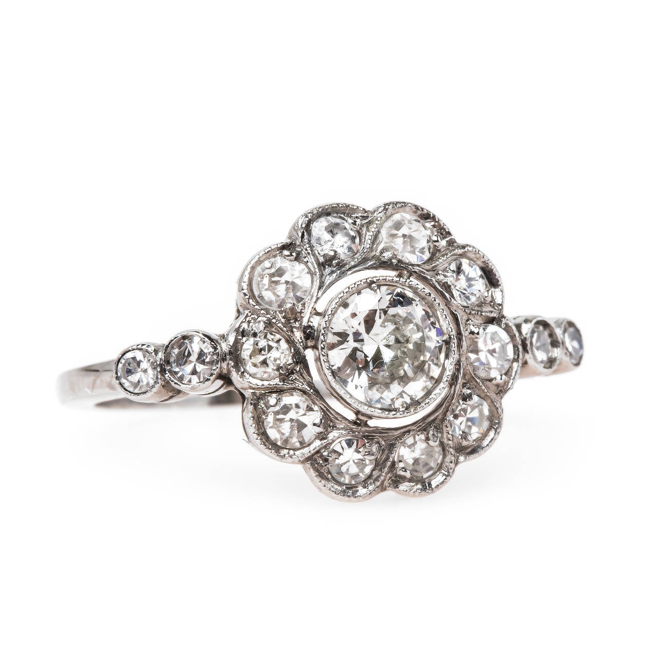 Old Portsmouth is an alluring authentic Edwardian era (circa 1910) platinum halo style ring centering a single bezel set Old European Cut diamond gauged at 0.25ct graded G-H color and VS2 clarity. A lovely halo of ten Single Cut diamonds totaling