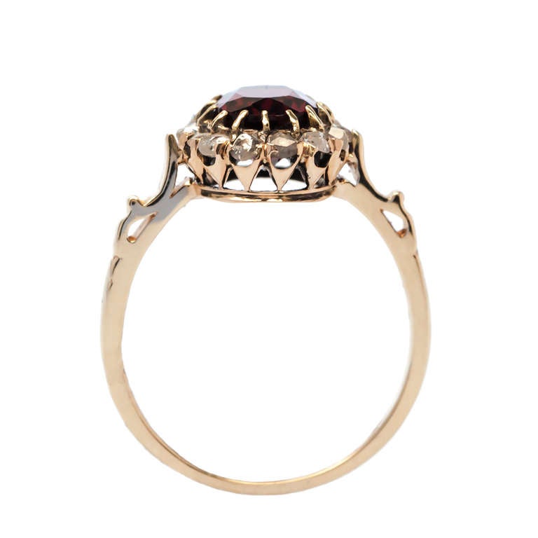 Elk Ridge is a whimsical antique Victorian era engagement ring made from 14k yellow gold centering an oval deep brownish red garnet gauged at approximately 1.75ct. The center garnet rests within a fifteen prong setting and is surrounded by fifteen
