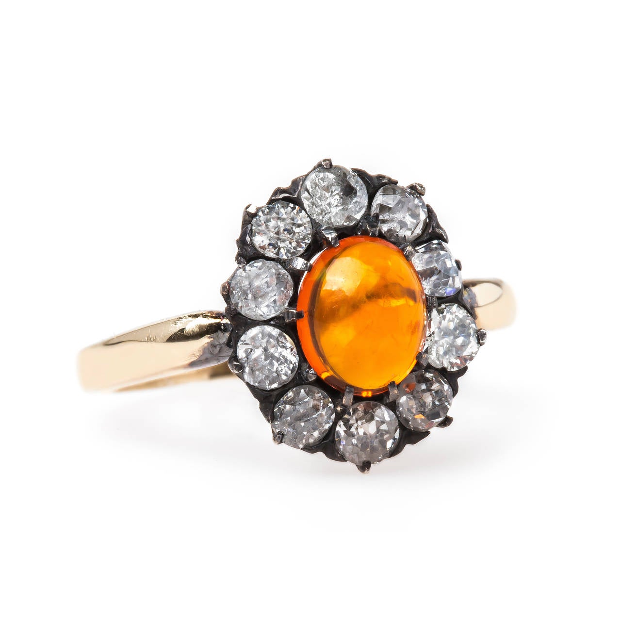 Orange Grove is a dazzling authentic Victorian (circa 1880) era silver topped 14k yellow gold ring centering an oval Cabochon fire opal gauged at 0.55ct. The gleaming stone is framed by a sparkling halo of ten Old Mine Cut diamonds totaling