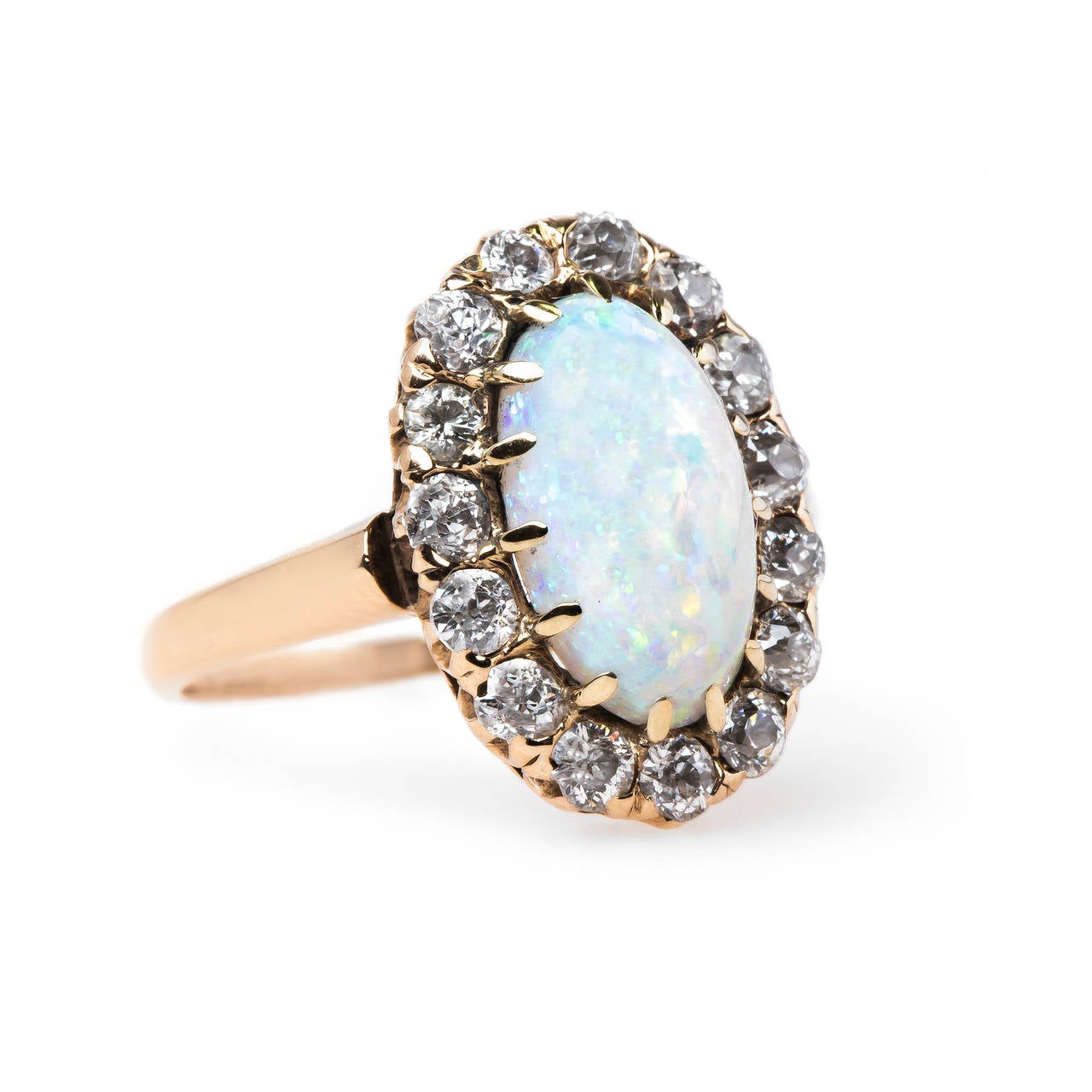 Crestwood is an alluring Victorian era (circa 1900) 14k yellow gold ring centering an elongated Oval cabochon white opal. The dreamy stone is gauged at 10.5mm x 6mm and glows warmly with a sweet rainbow play-of-color. Crestwood is further framed by