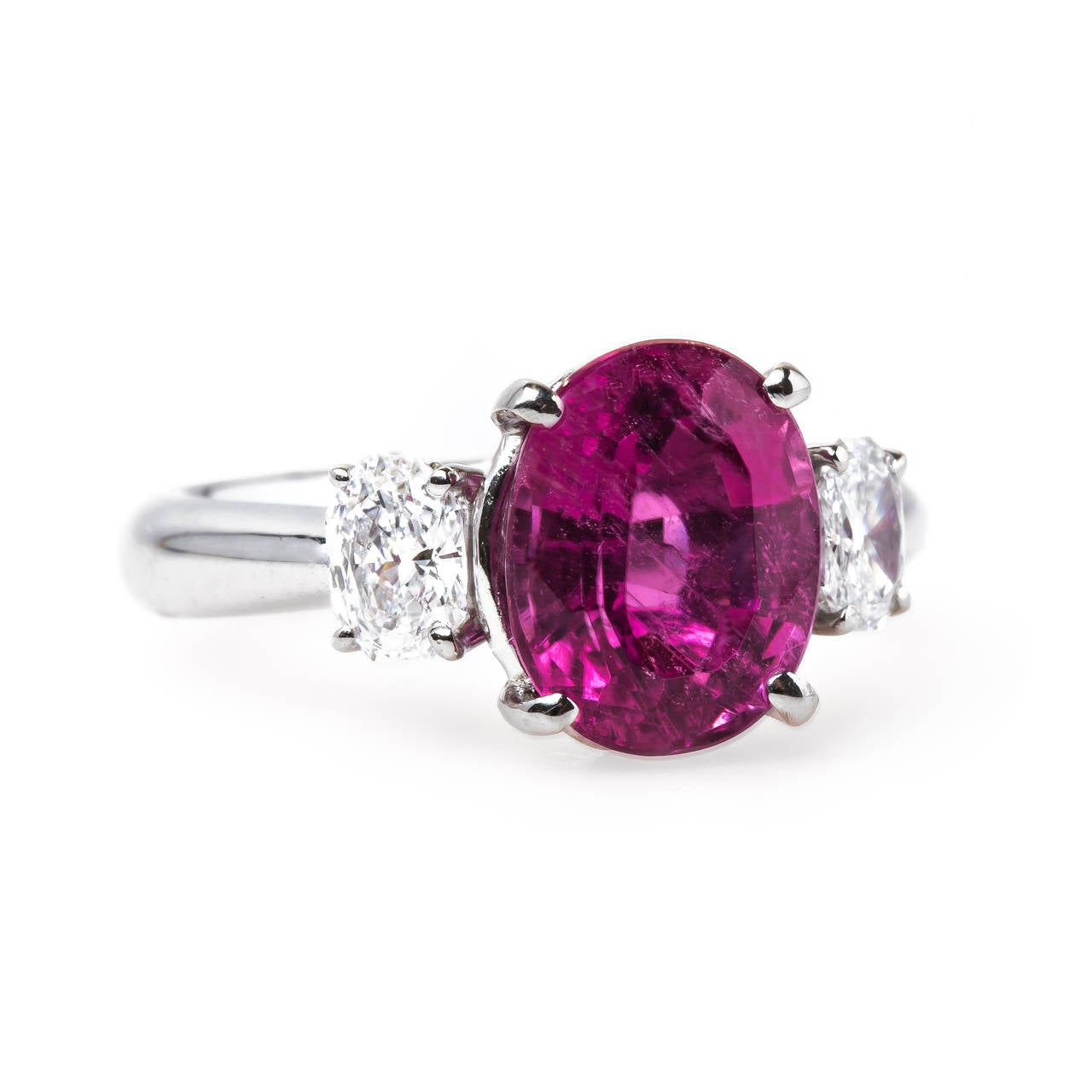 Bixby Bridge is a bright and beautiful modern (circa 1990) platinum ring centering a four-prong set neon Oval Cut natural pink tourmaline with an exact weight of 3.00ct. The stunning pink stone is flanked by two uniquely shaped Oval Octagonal Cut