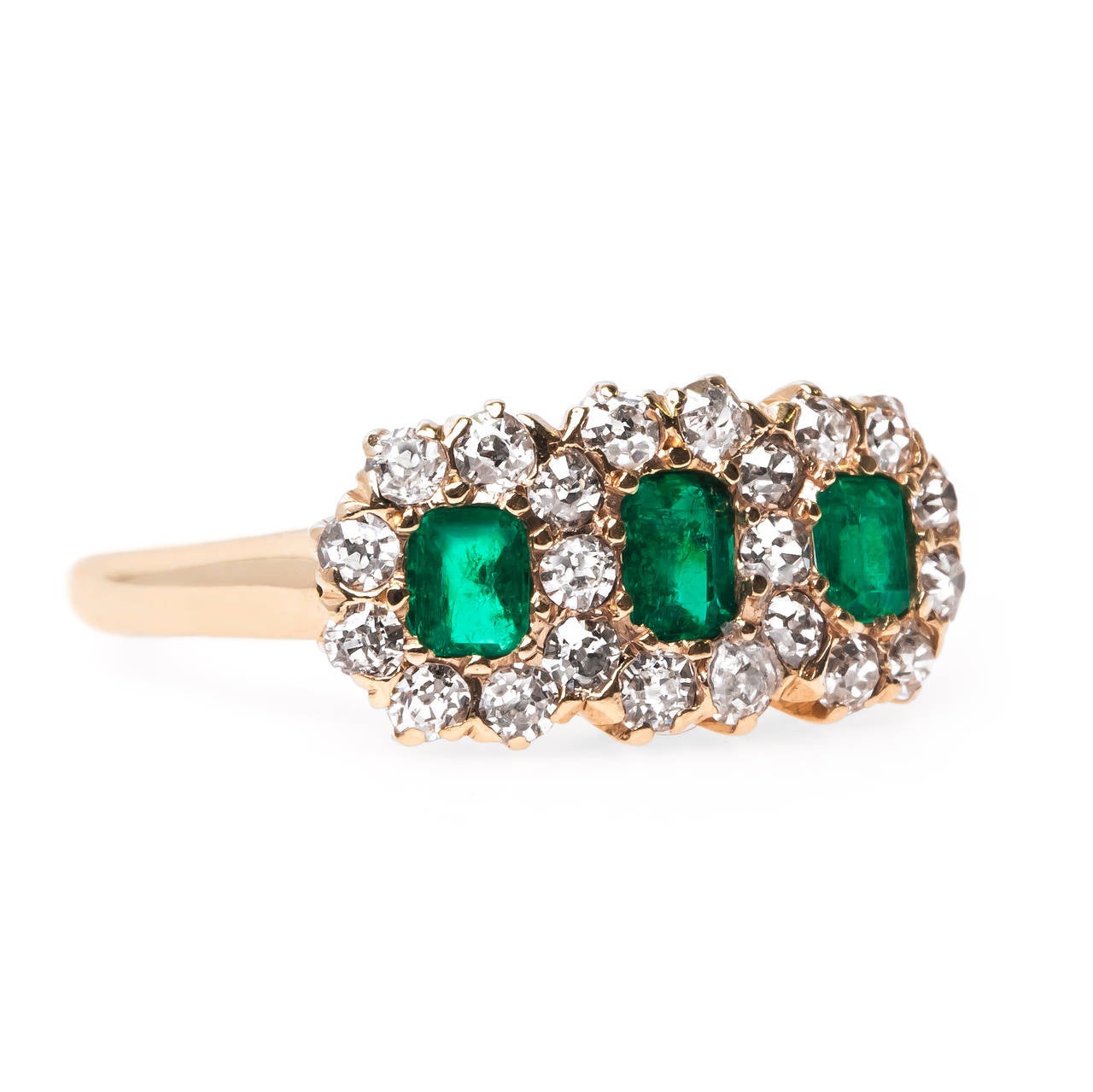 Columbus Circle is a dramatic Late Victorian (circa 1900) 14k yellow gold ring centering three intensely saturated natural Rectangular Step-Cut emeralds totaling approximately 0.55ct total weight. The emeralds are slightly abraded on the top due to