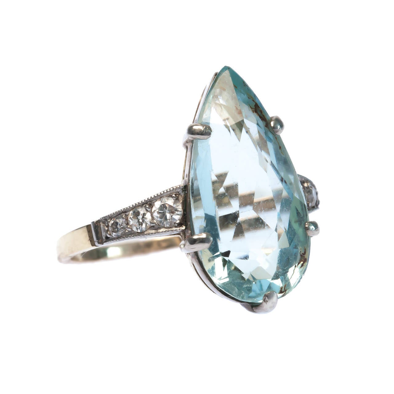 Seychelles is a striking Late Art Deco platinum topped 18k yellow gold ring centering a four prong set 5.78ct pear shaped aquamarine flanked on either side by six Old European Cut diamonds totaling approximately 0.20ct. Seychelles is delicately