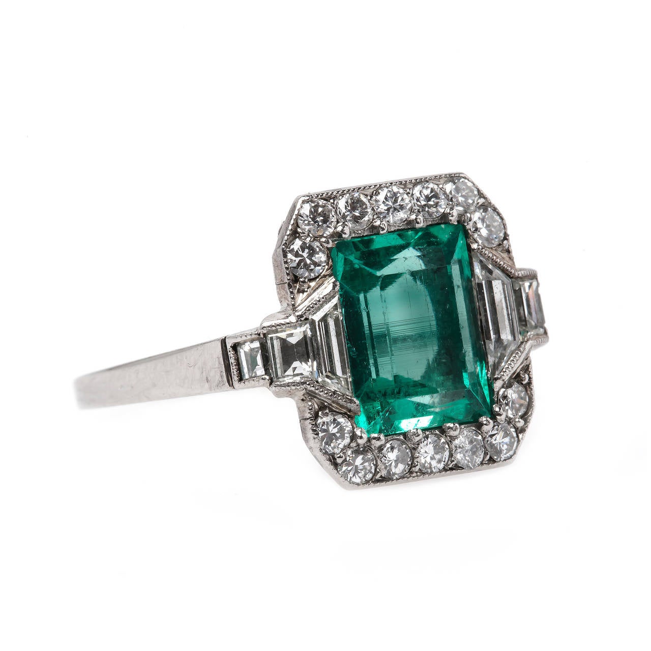 Autry Trail is a timeless authentic Art Deco (circa 1925) platinum ring centering a prong set Rectangular Step cut natural Colombian emerald gauged at 1.85 carat accompanied with a Guild Laboratories Certificate. This perfectly saturated green color