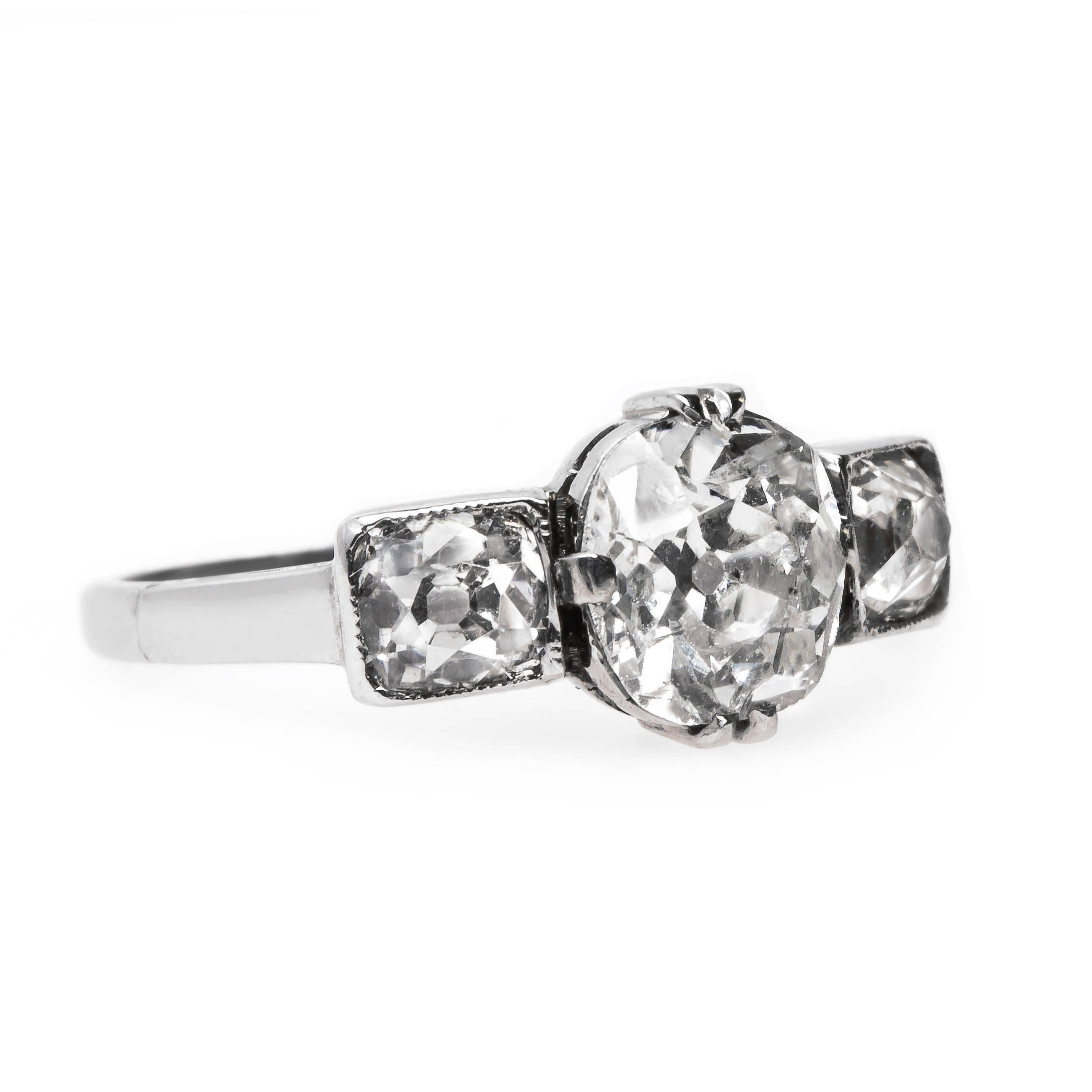 Cobble Hill is a fantastic and authentic early Edwardian era (circa 1905) platinum engagement ring featuring the classic three-stone combination. The ring centers a talon and single prong set 1.04ct EGL certified Old Mine Cushion Cut diamond graded