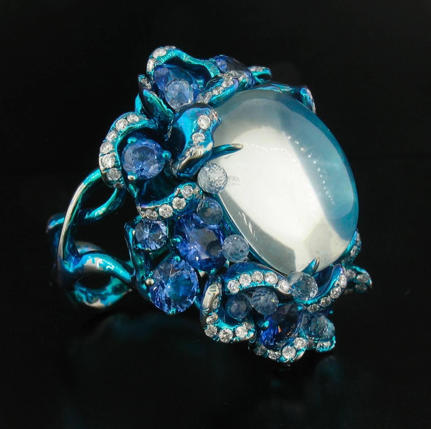 Dieser handgefertigte:: außergewöhnliche Ring wurde von dem berühmten Designer Arunashi entworfen und enthält einen extrem reinen blauen Mondstein von höchster Qualität mit einem Gewicht von 20::70 Karat.  Er ist umgeben von 13 Ceylon-Saphiren mit