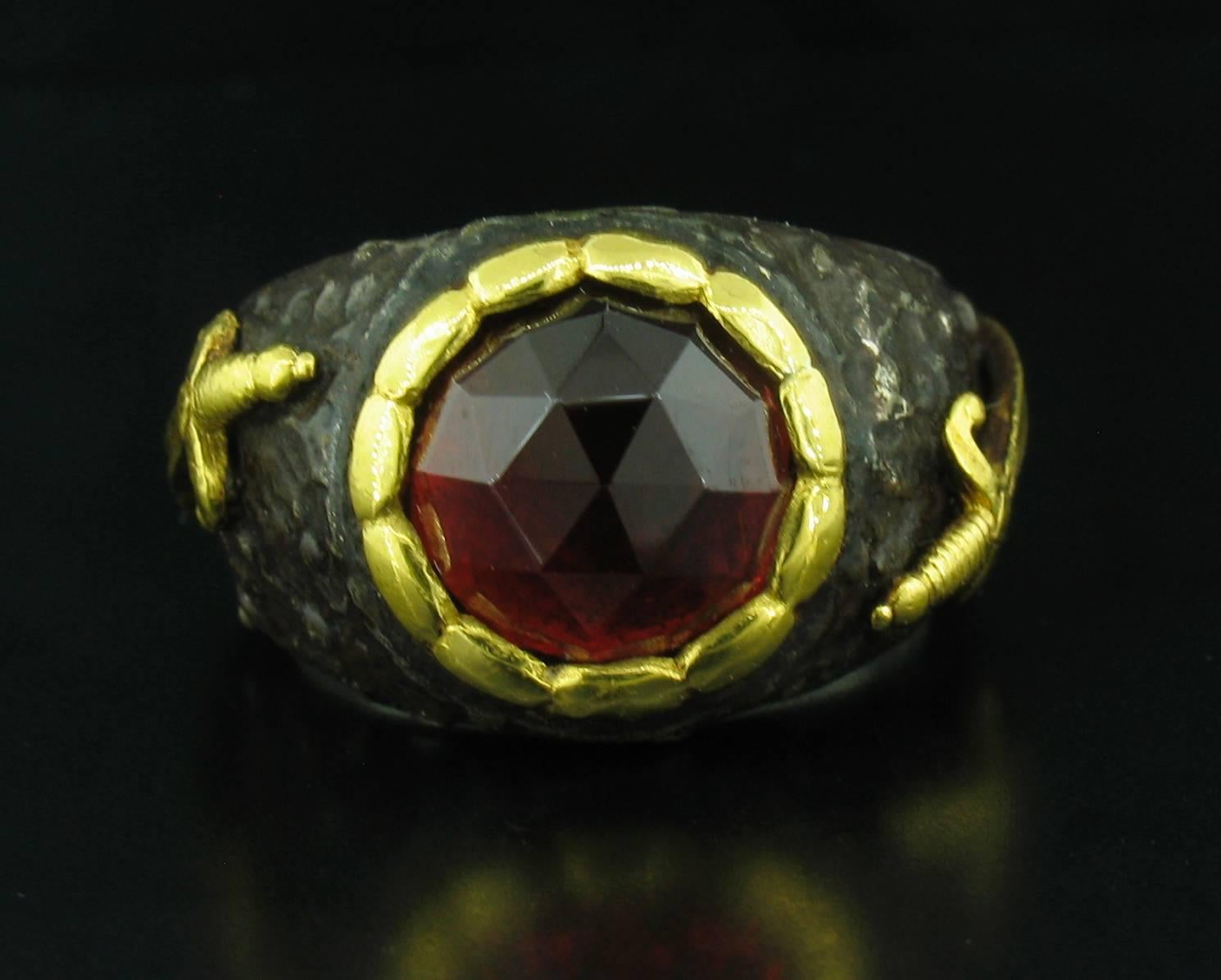 This ring was designed and made by well known designer Victor Veylan. It contains a beautiful warm red, faceted, round Garnet weighing 3.15 carats, which has been reverse set.  It is made of a base of pure Silver with all accent work created in 24k