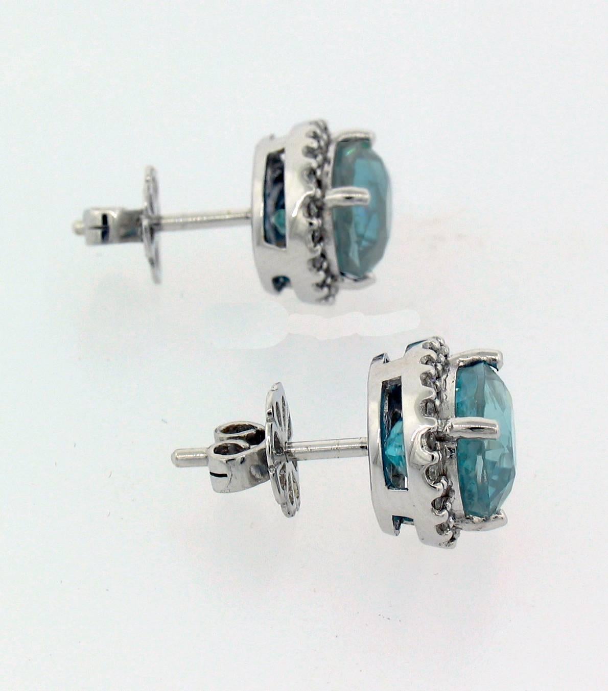 Natural Cambodian Blue Zircon stud earrings feature oval blue zircons weighing a total of 8.15 carats with a diamond halo weighing a total of 0.37 carats.  Set in 14k white gold, they measure 1/2" long x 7/16" wide x 5/16" deep.