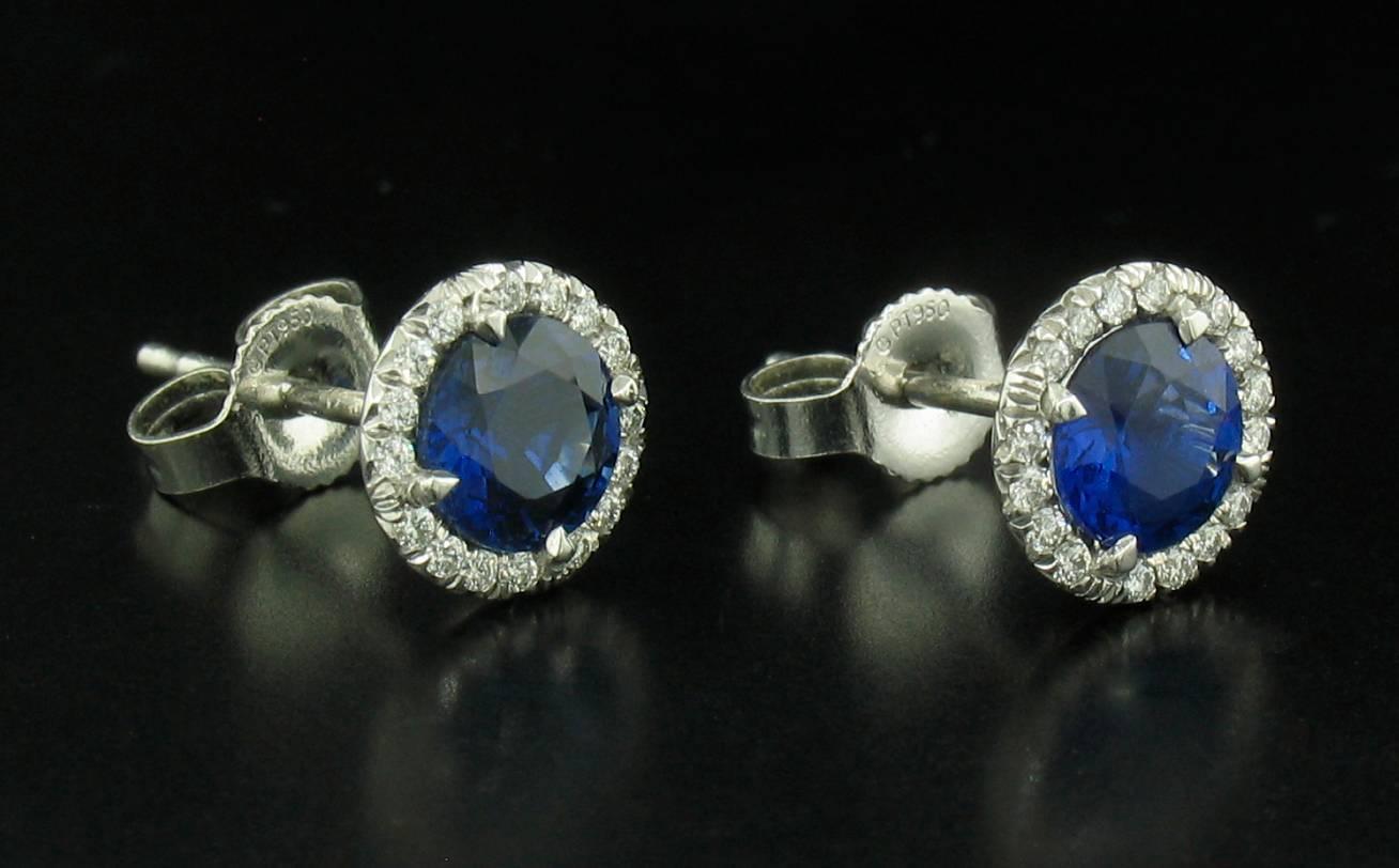 Sapphire stud earrings feature round sapphires weighing a total of 1.14 carats with a diamond halo of 32 Diamonds weighing 0.10 carats.  These are handmade platinum settings.  Variations in sapphire color are a result of reflection in the camera -