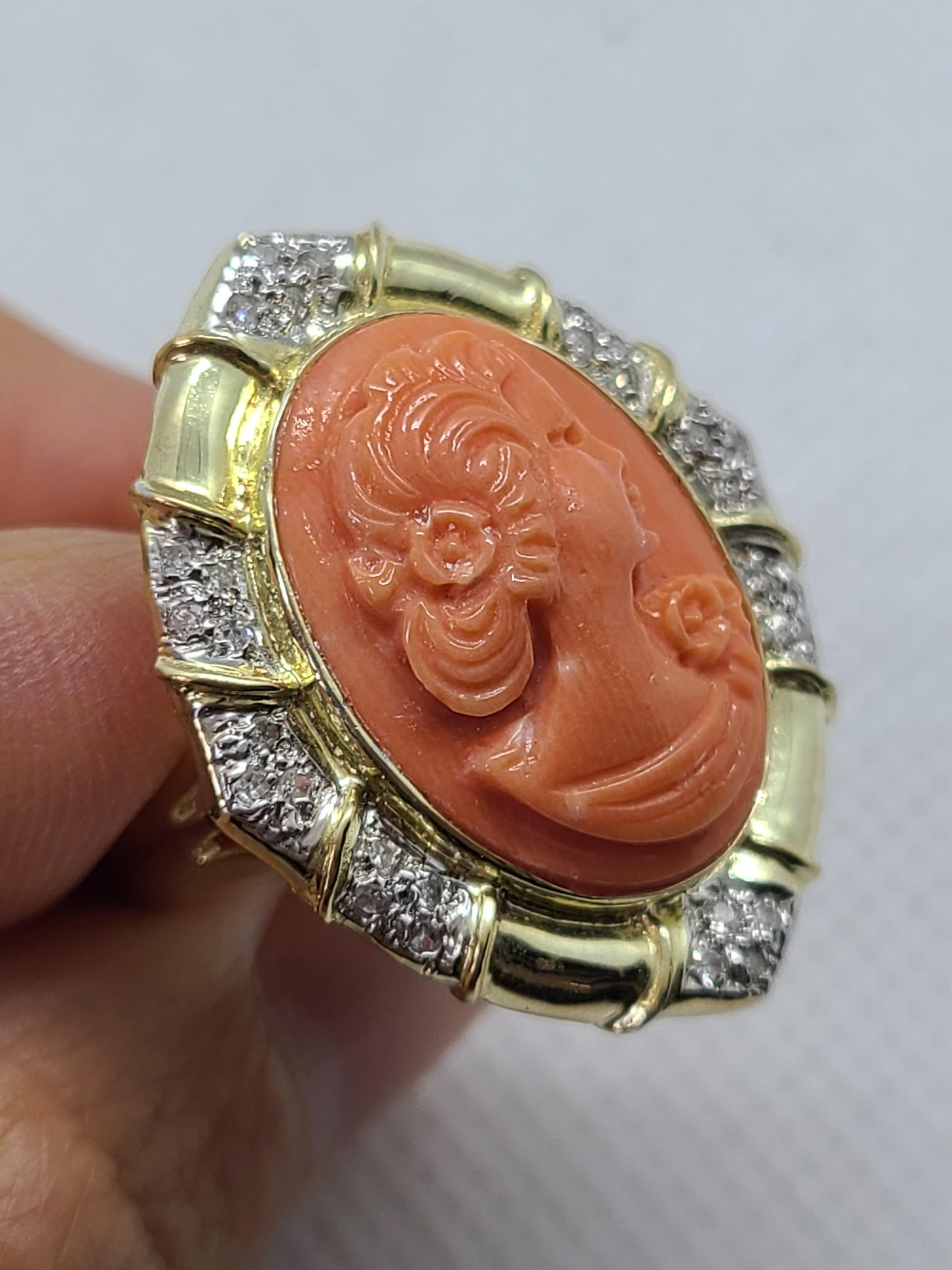 Cette pièce exceptionnelle présente le portrait d'une dame finement sculpté à la main dans un corail naturel de couleur rose-orange, encadré de diamants ronds brillants. Sertie en or jaune 14 carats, cette élégante bague est d'une taille