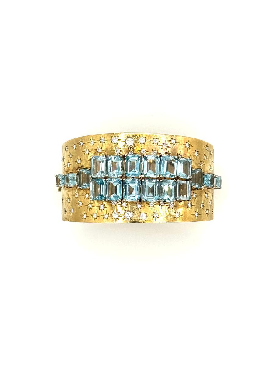Ce bracelet bangle vintage en or jaune 18 carats est une pièce audacieuse et glamour. Il présente 18 magnifiques aigues-marines de taille émeraude serties en trois rangs sur une large manchette en or texturé. Accentué par des diamants ronds épars de