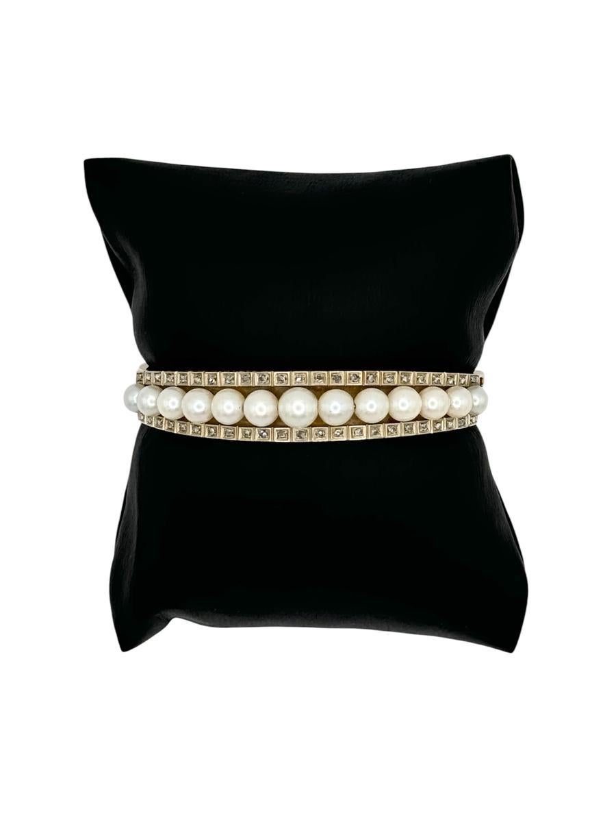 This elegant antique bangle is crafted in 14 karat yellow gold and showcases a central row of 13 graduated cultured pearls, ranging in size from approximately 7.05mm to 5.2mm. Flanked on either side are two rows of 46 rose-cut diamonds (92 total),