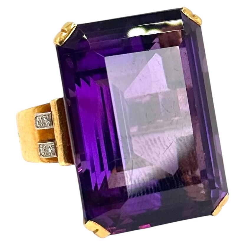 Ein beeindruckender Ring der Retro-Ära aus den 1940er Jahren mit einem massiven tiefvioletten Amethysten im Smaragdschliff in einer klassischen 4-Zacken-Fassung. Das breite Band aus 18 Karat Gelbgold ist mit vier runden Diamanten verziert, die den