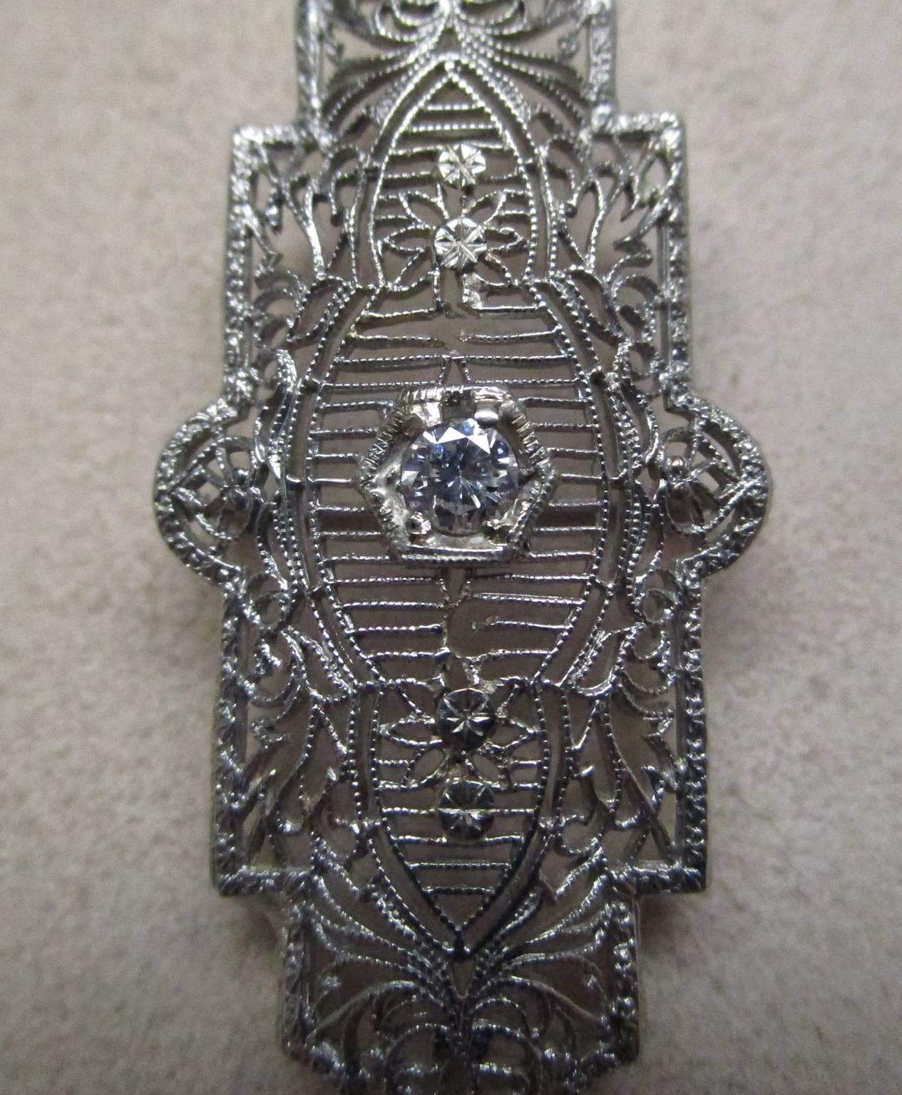 This exquisite piece is a pendant as well as a pin. The long, geometric details are exemplary qualities of the Art Deco period from which this 14 karat white gold piece originates. It has a bail that allows it to be a functioning and versatile