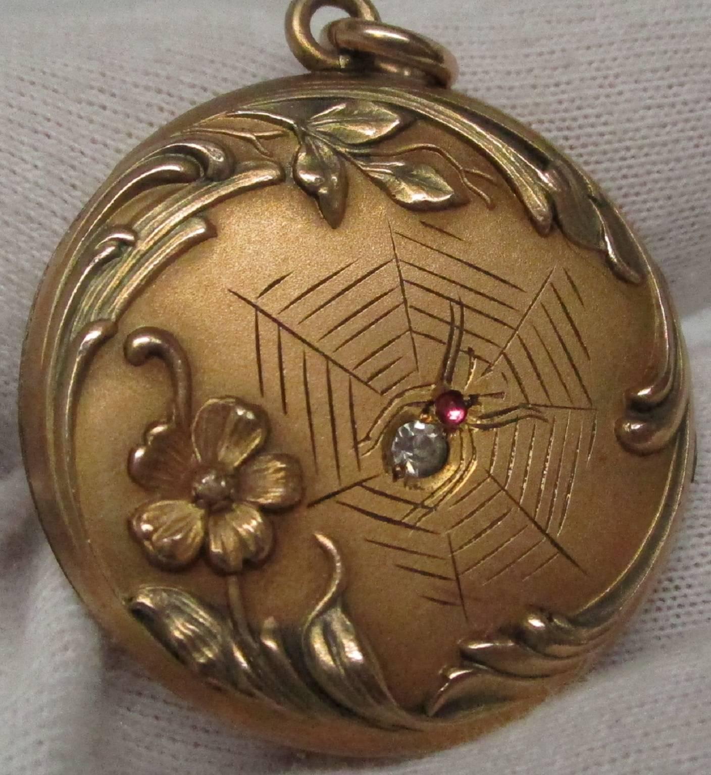 This is a beautiful gold filled Victorian locket with a spider and web motif. The spider is made up of a ruby cabochon for its thorax and a single cut diamond for the rest of its body, resting on an engraved web with a floral edging. Your friends
