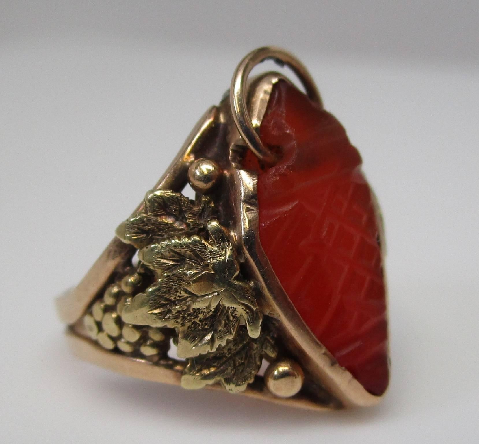 This wonderful 14K yellow gold ring is from the 1910 Arts and Crafts period. It features a craved carnelian with a loop though one end and grapes with leaves on the shoulders. It is not broken, it shows dissimilar oxidation as the solder was a