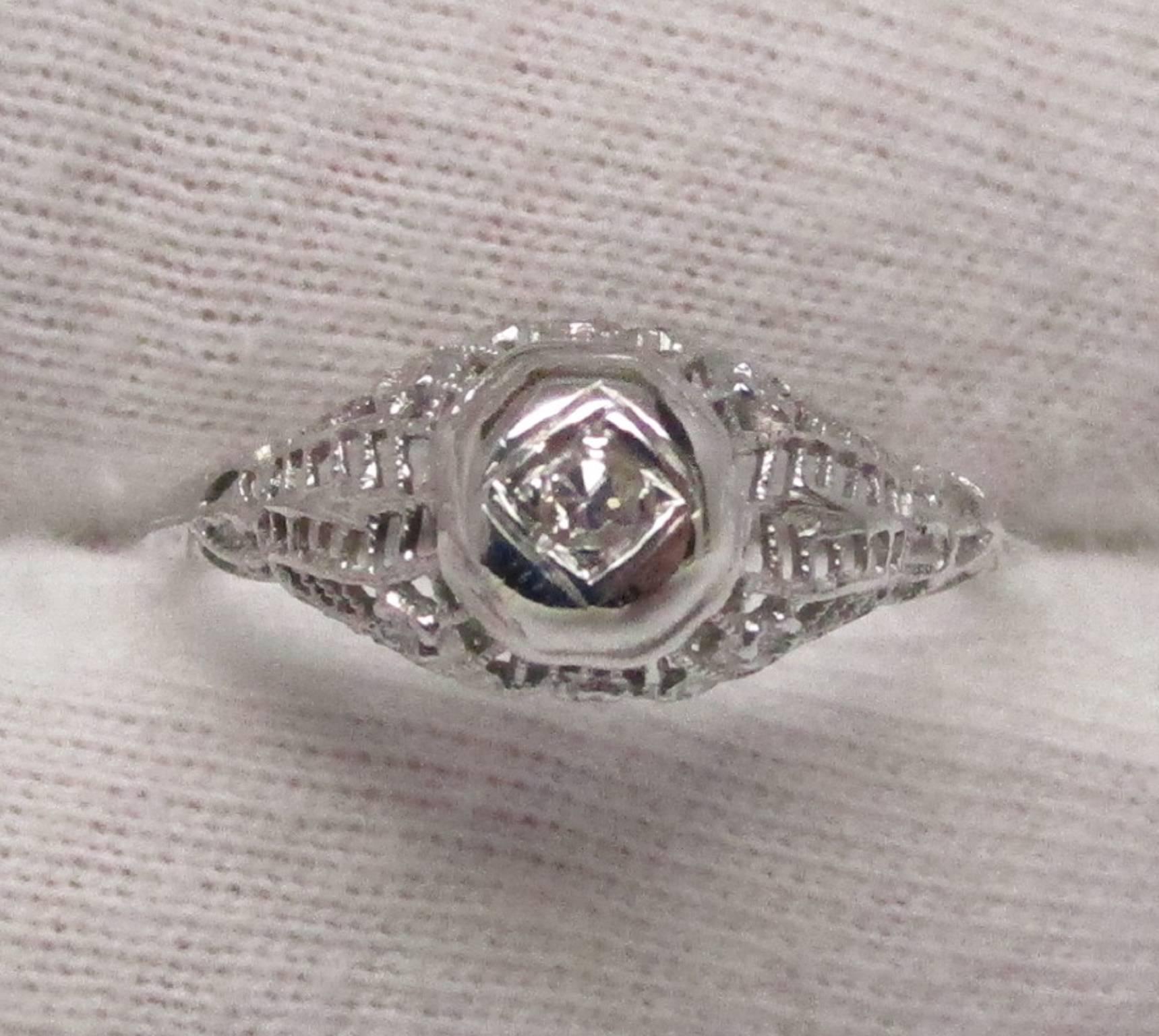 This stunning 18K white gold ring has everything you would want in a c. 1925 Art Deco Filigree diamond engagement ring. The ring is clean and crisp, showing no signs of wear. The 0.10ct diamond adds just the right amount of flash to be noticed, with