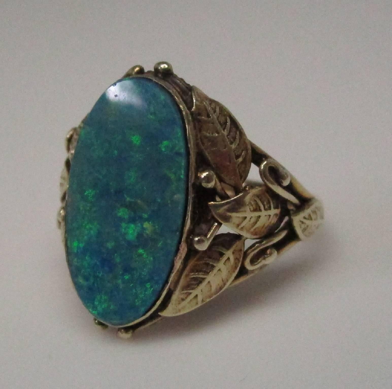 3.0 carat Boulder Black Opal set in Arts & Crafts ring in 14K yellow gold 
Exceptional shoulders with leaf design! Lovely opal - no dead zones, lots of blue and green fire. There is a small chip shown in the photos, it is barely noticeable when just