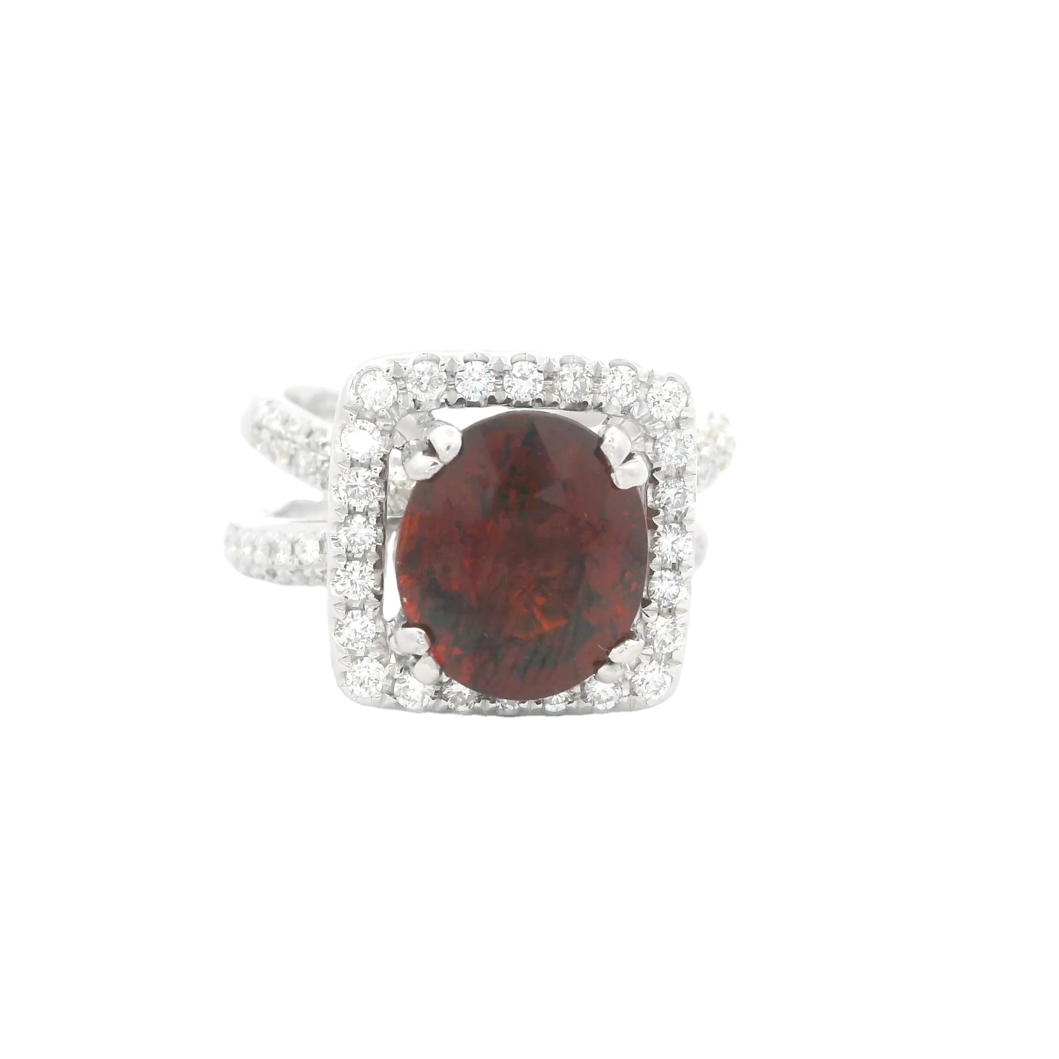Questo anello da cocktail contemporaneo è realizzato in oro bianco 18 carati e presenta un vivido granato dal taglio ovale del peso di circa 4,00 carati. La gemma rosso intenso è incorniciata da una scintillante aureola di diamanti rotondi a taglio