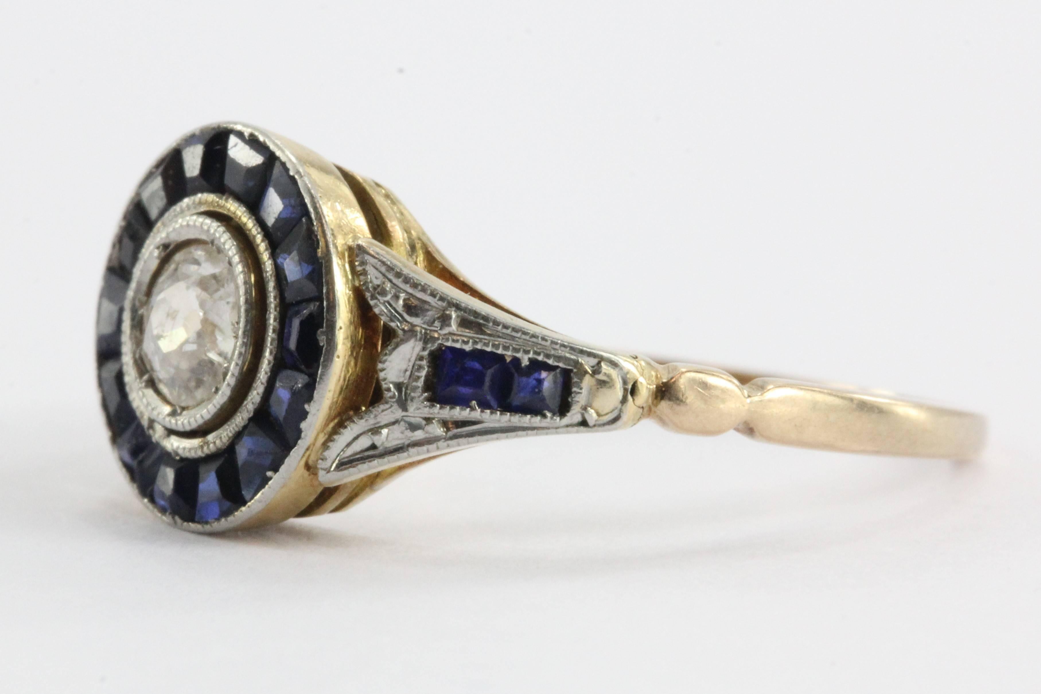 Art Deco Diamond and Calibre Blue Sapphire 18K Gold with Detailed Platinum Design Engagement Ring, Approximate Size US 6.25

The center diamond is a .20 carat Si1, G-H color old mine cut bezel set around 14 calibre blue sapphires. Due to age, two