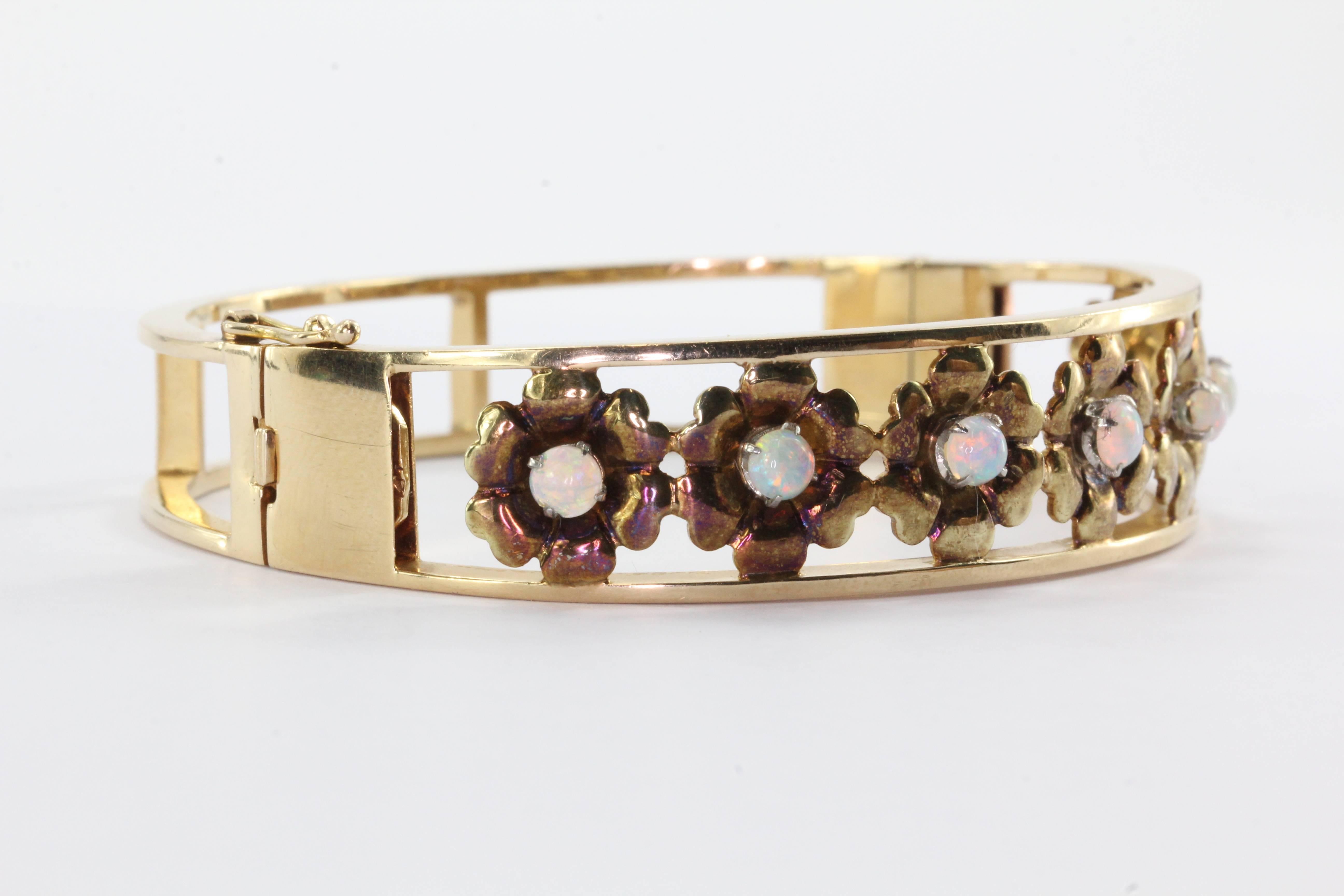 Retro 1960's 14K Yellow Gold Opal Floral Bangle Bracelet. The bracelet is in excellent estate condition and ready to wear. It is hallmarked 14K on the clasp. The clasp and safety clasp both work perfectly. The seven opals have gorgeous play of