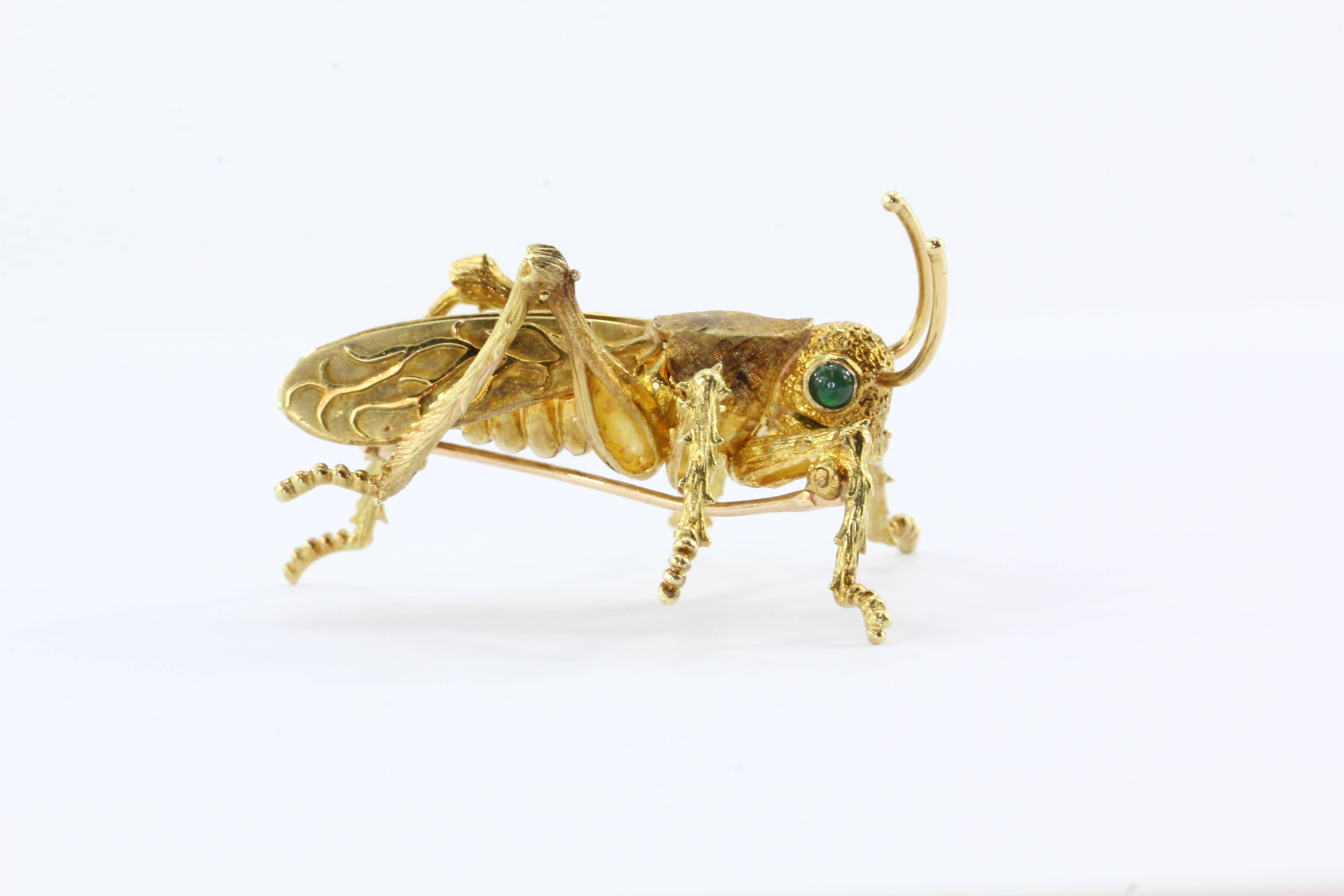 18K Yellow Gold Emerald Kurt Wayne Naturalistic Grasshopper Brooch Pin. The piece is in excellent estate condition and ready to wear. It is marked with the serial number 54377 on the bottom. The eyes are set with genuine emerald cabochons. The piece