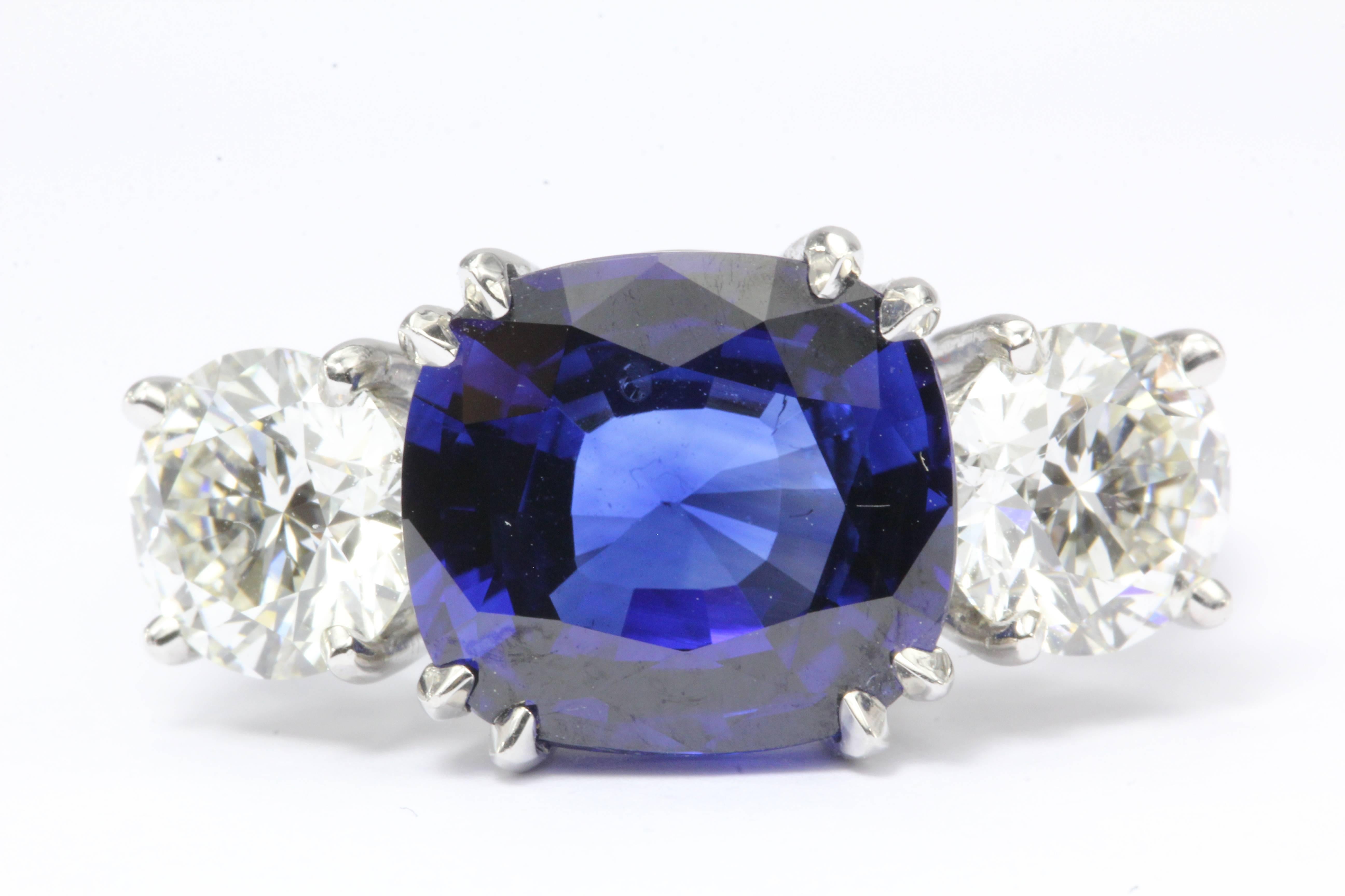 A stunning and beautiful engagement ring is set with a large brilliant vivid blue sapphire. The setting is platinum, the natural blue sapphire is 4.75 carats (10.58 x 9.64 x 5.05mm) and flanked by two 1 carat round brilliant diamonds (2 carats total