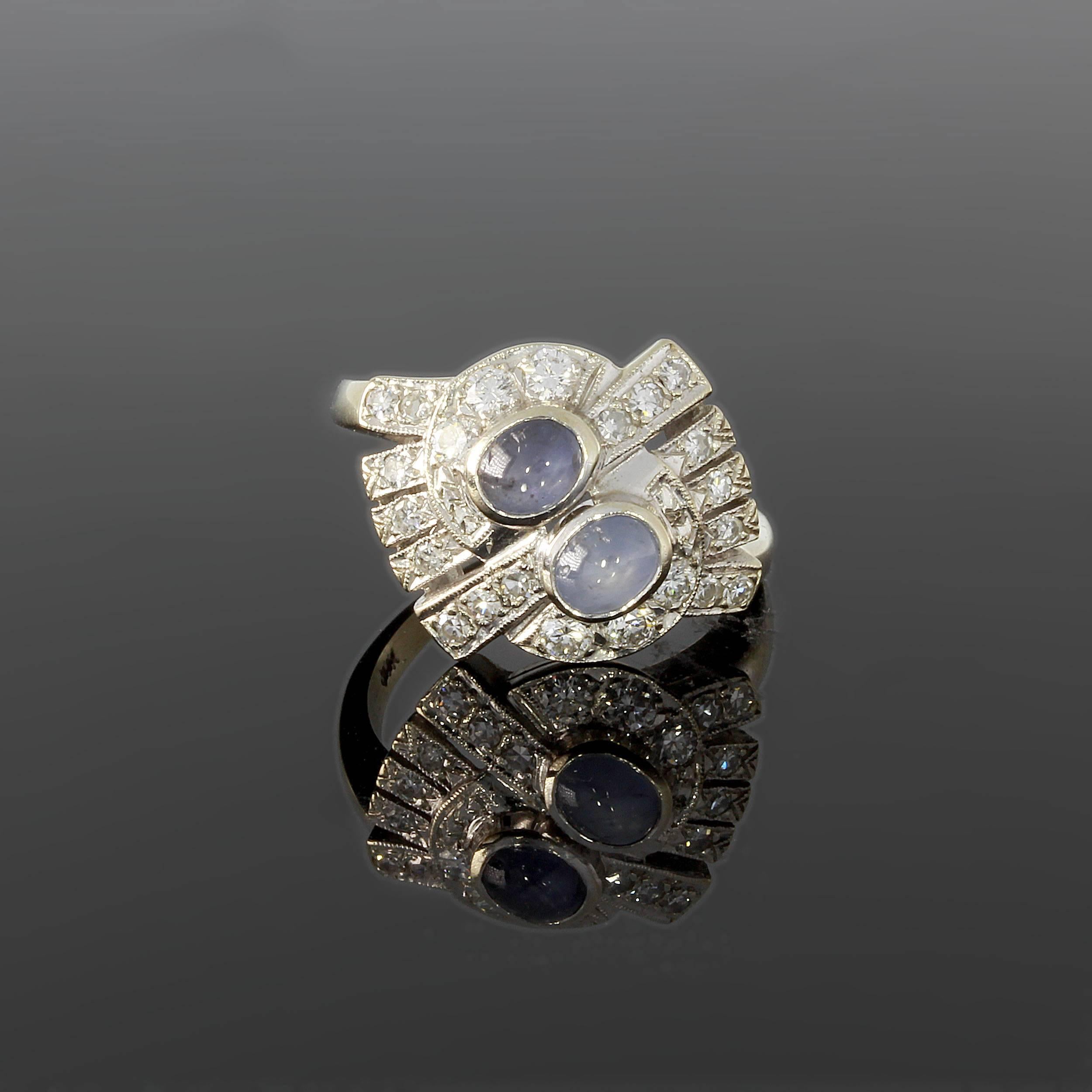 USA, 1930's. 2 blue star sapphire in cabochon-cut surrounded by 28 brilliant-cut diamonds weighing circa 0.71 ct. Mounted in 18K white gold. Millegrain setting. Hallmarked inside. circa 0.59 x 0.71 in ( 1,5 x 1,8 cm ). Total weight: 5,99 g. Ring