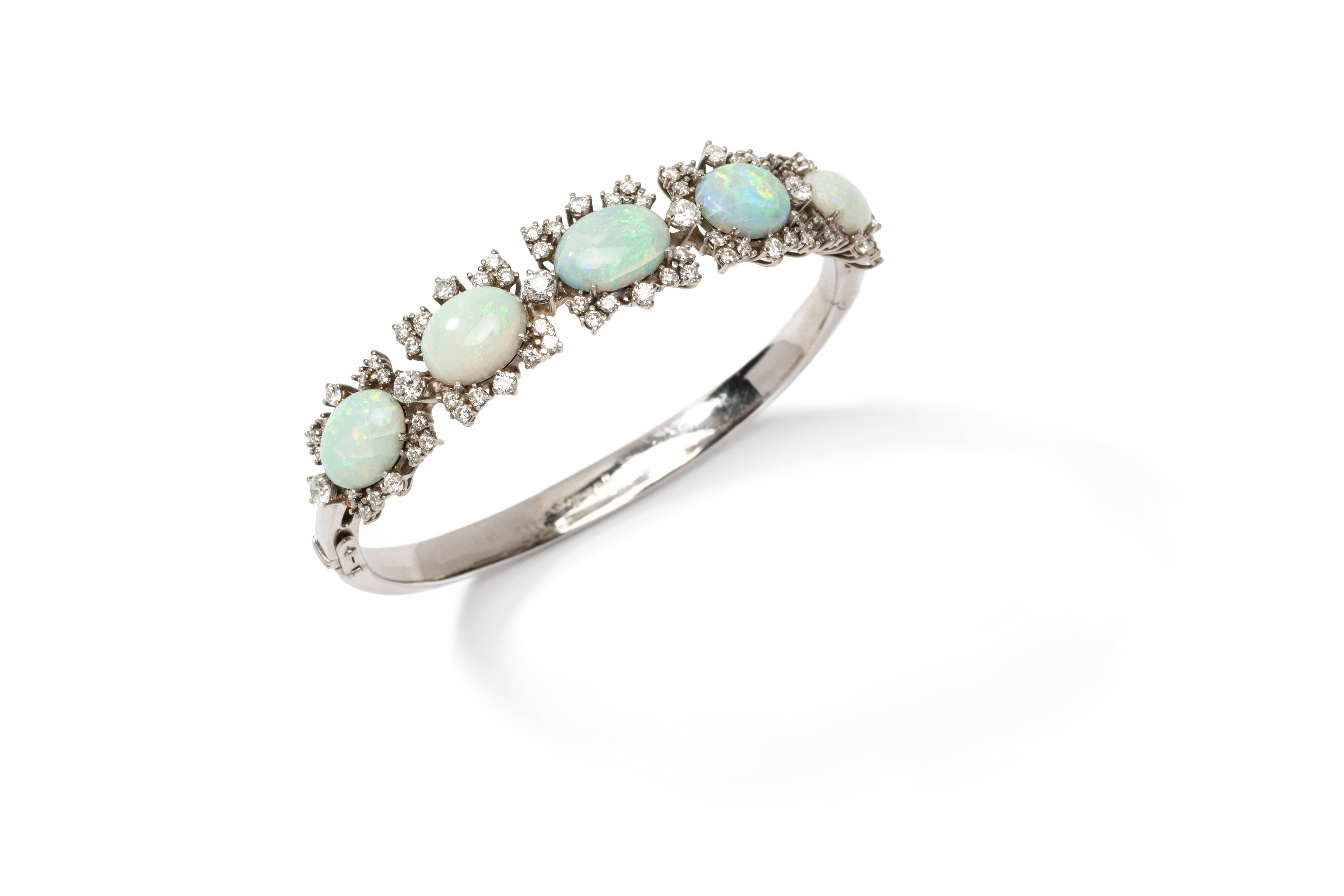 Fashionable jewelry creation by Jeweler Hohenberger. Oval bangle with elevated front. 5 opal cabochons weighing total circa 20,00 carats, surrounded by 76 brilliant-cut diamonds weighing ca. 3,36 ct., VS, wesselton. Mounted in 18 carat white gold.