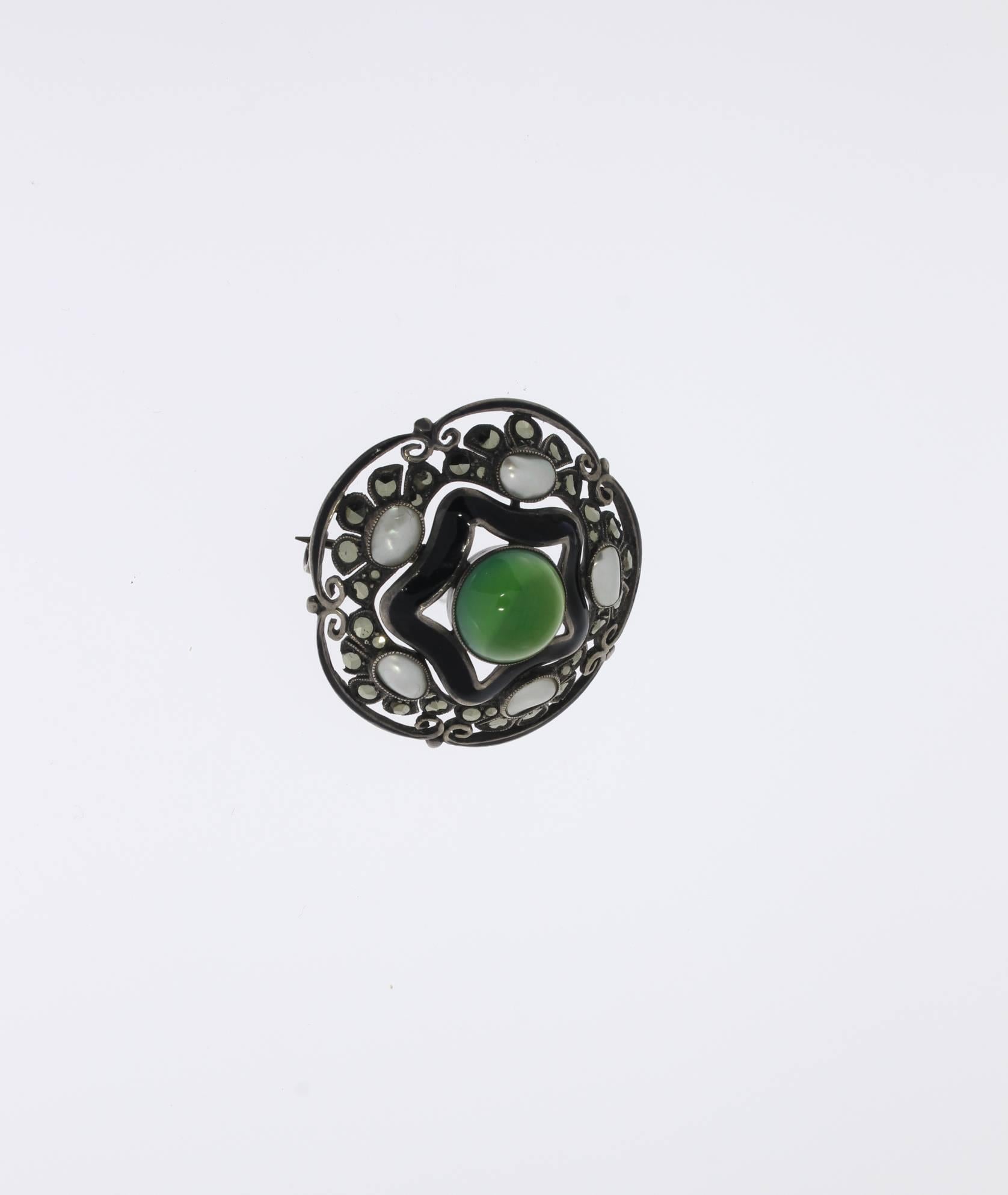 This brooch is typical for Theodor Fahrner’s silversmithing. Geometric form and contrasting colours. Center set with a chrysoprase decorated by marcasites, mother-of-pearl and black enamel. Mounted in silver. 
Marked on the back: GERMANY STERLING.