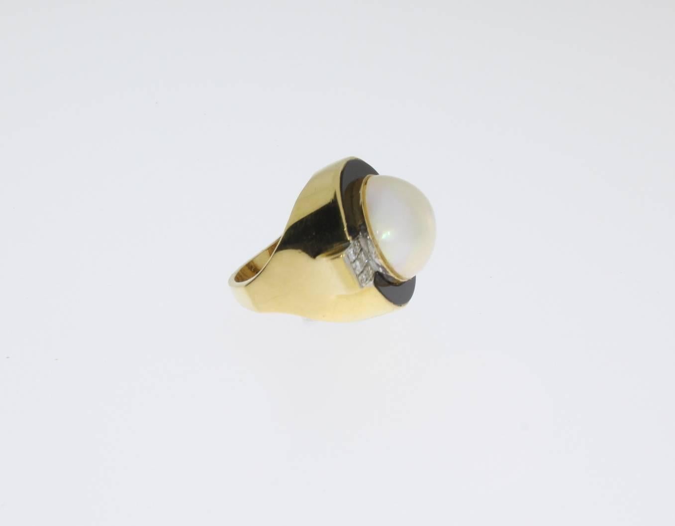 The ring is crafted in 14K yellow gold. A large mabé pearl is captured within an round setting that is further provided with an onyx and 12 brilliant-cut diamonds weighing ca. 0,24 ct. Marked on the ring band with the purity 14K. Total weight: