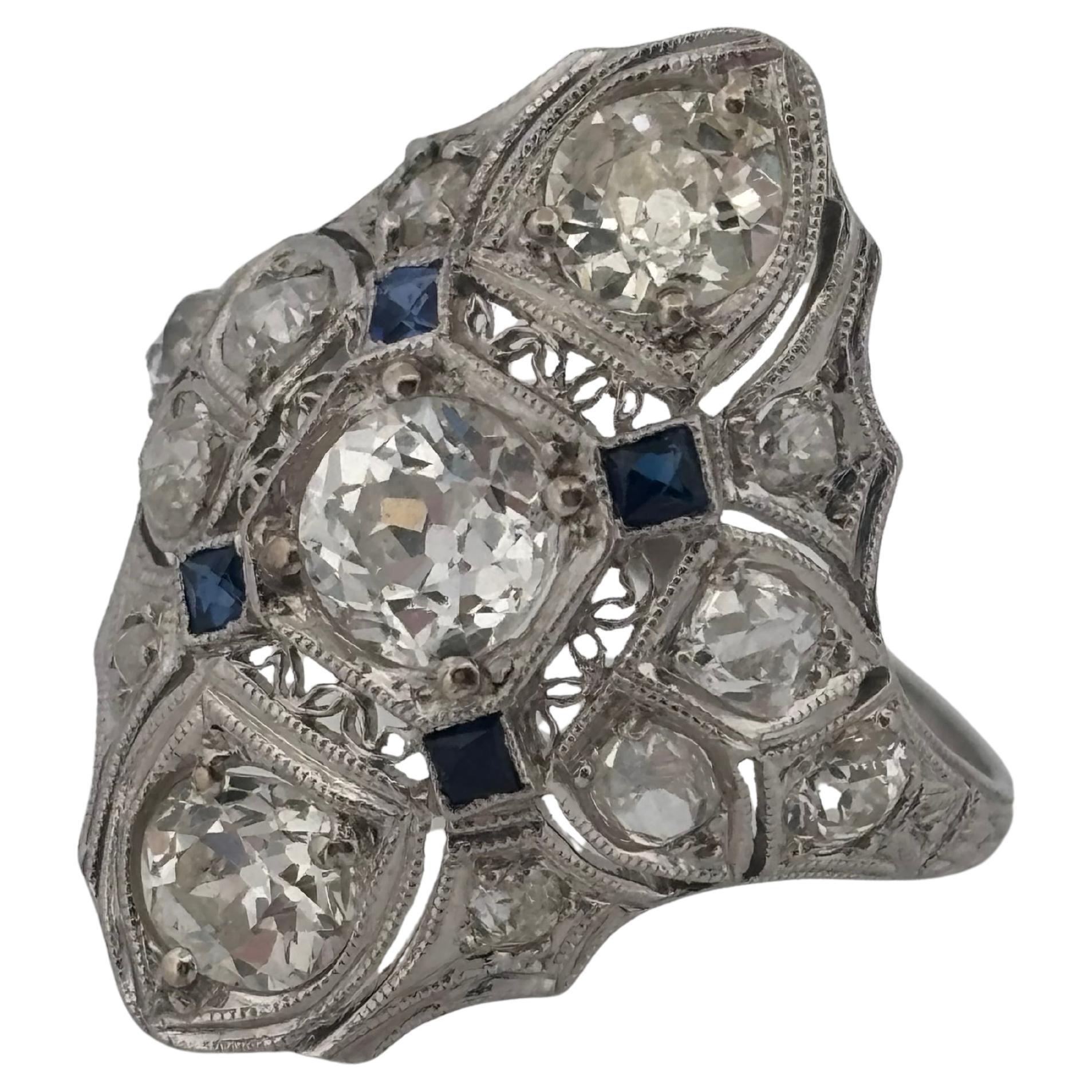 This ring is a magnificent example of 1920s art deco craftsmanship. The platinum ring features a striking geometric design adorned with diamonds and sapphires. At its center is a sparkling Old European cut diamond, flanked by additional antique