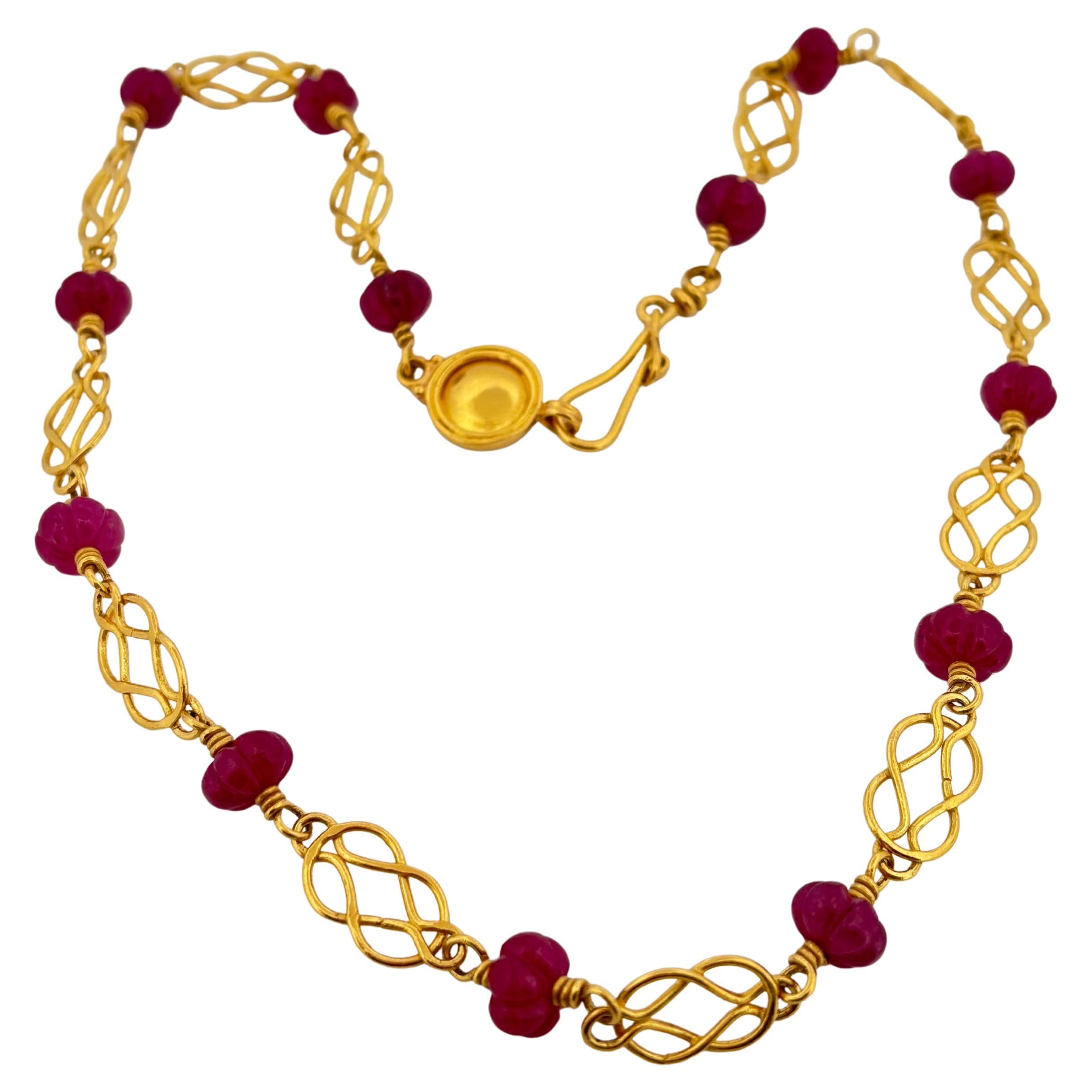 This exquisite necklace by Bessie Jamieson is handcrafted in rich 22k yellow gold and showcases a delicate interplay of artistry and elegance. Featuring intricately carved ruby beads, each gemstone is uniquely shaped, exuding warmth and vibrant