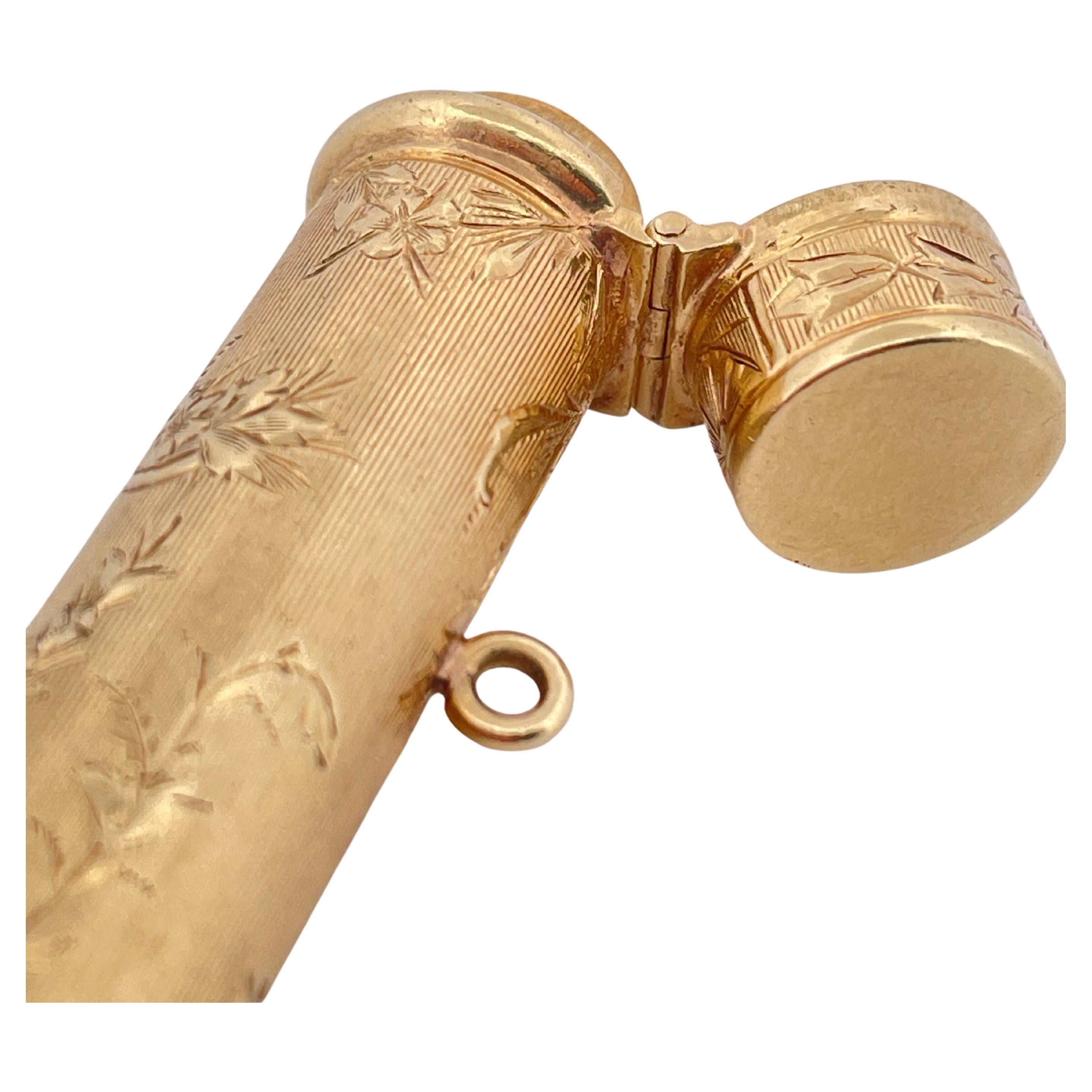 This elegant vintage lipstick holder is crafted in richly engraved 14k yellow gold, showcasing exquisite floral and neoclassical motifs throughout its cylindrical form. The detailed hand-engraving features a basket of flowers on a vertically lined