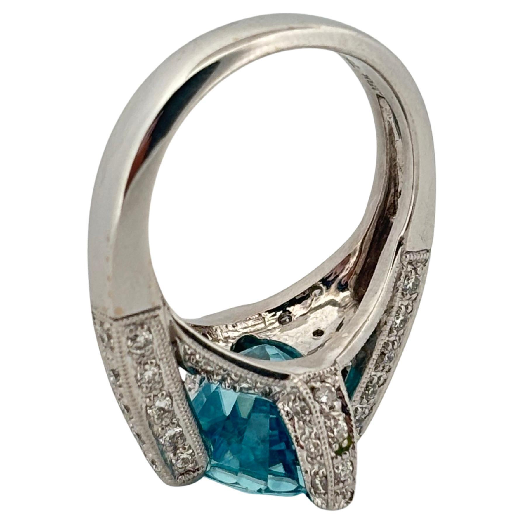Crafted in luminous 18k white gold, this captivating ring weighing 10.2 grams, showcases a mesmerizing 7.00 carat oval-cut blue zircon, celebrated for its vibrant brilliance and extraordinary fire. The richly hued centerpiece is secured by four
