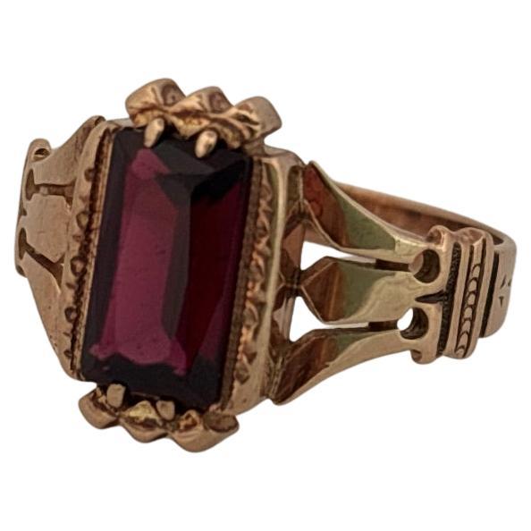 Cette exquise bague ancienne est réalisée en or rose 10 carats et met en valeur un grenat d'un rouge profond. Le grenat, taillé en forme d'émeraude élégante, présente une teinte riche, semblable à celle du vin, qui reflète la lumière avec un éclat