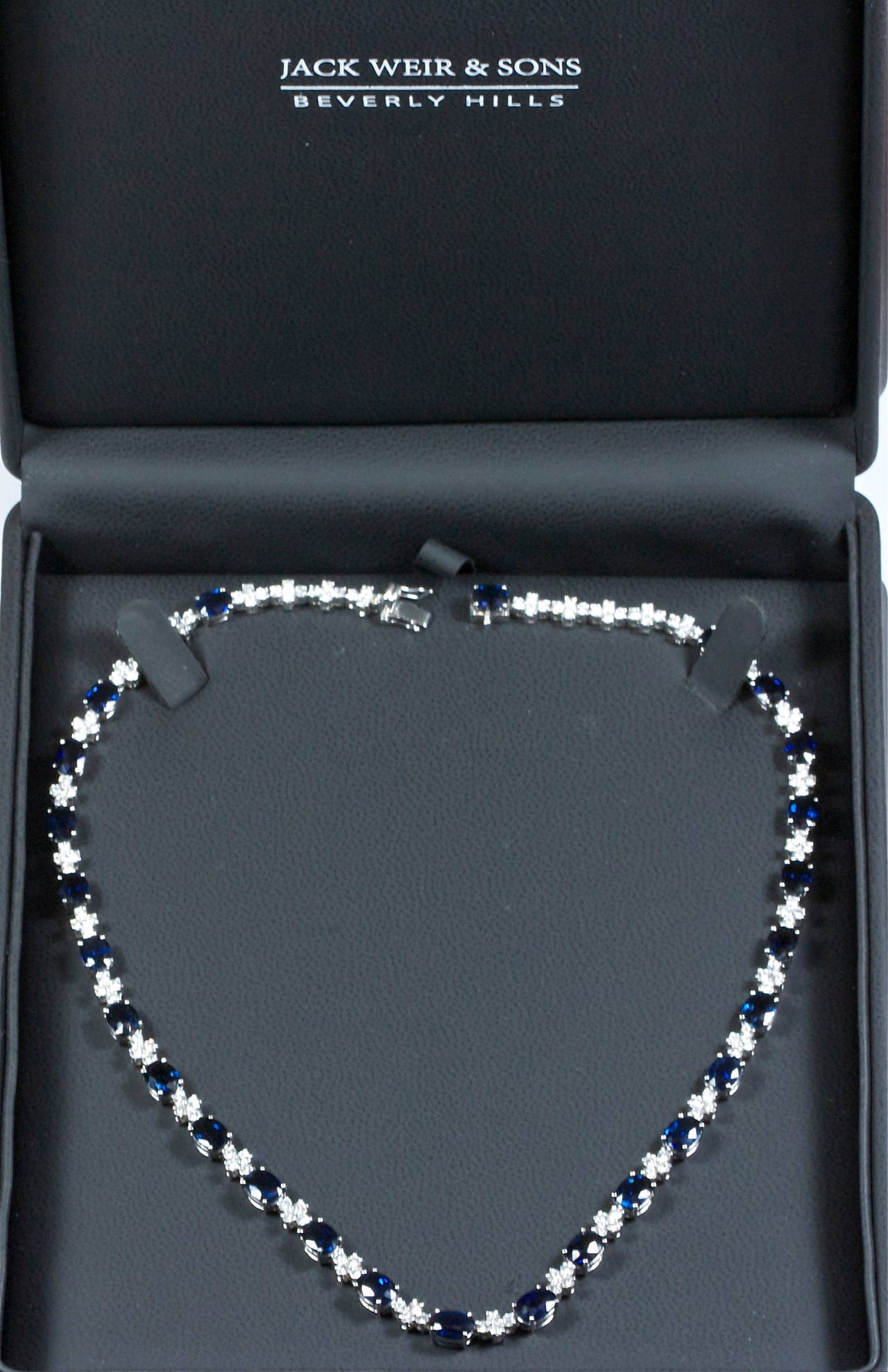 The elegant 18k white gold necklace has been designed with 27 oval sapphires weighing 26 carats. The deep blue sapphires are perfectly spaced and accented by 4.32 carats of white, clean round cut diamonds. Well made and easy to wear.