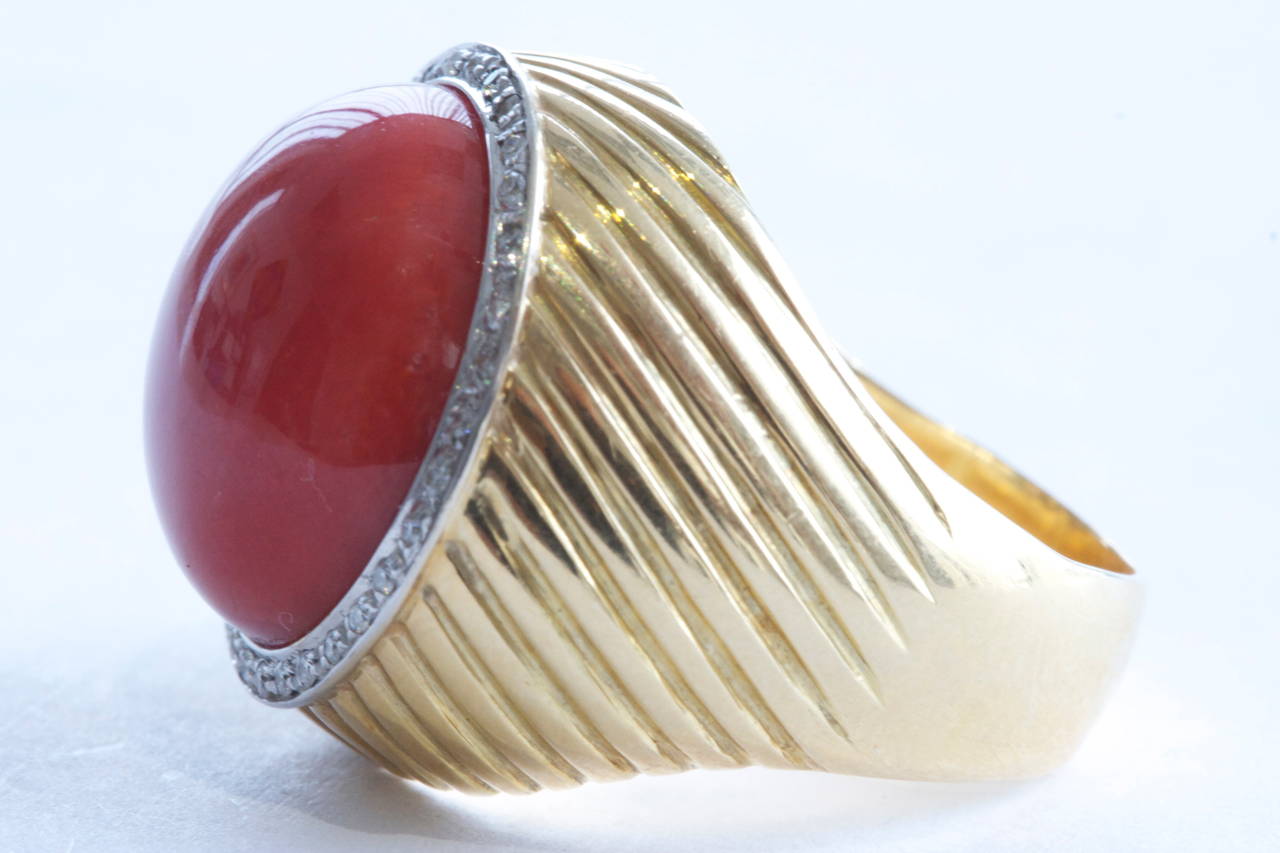 The color you aspire and desire for in coral. The ring features a cabochon ox blood coral surrounded by a single row of diamonds that is accented by contoured engravings. In 18k yellow gold.