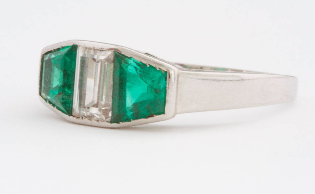 A fabulous French creation that is aesthetically pleasing in color and design. Featuring two bright green trapezoidal Colombian emeralds that sandwich a white emerald cut diamond that is E, F in color and VVS in clarity. The emeralds weigh