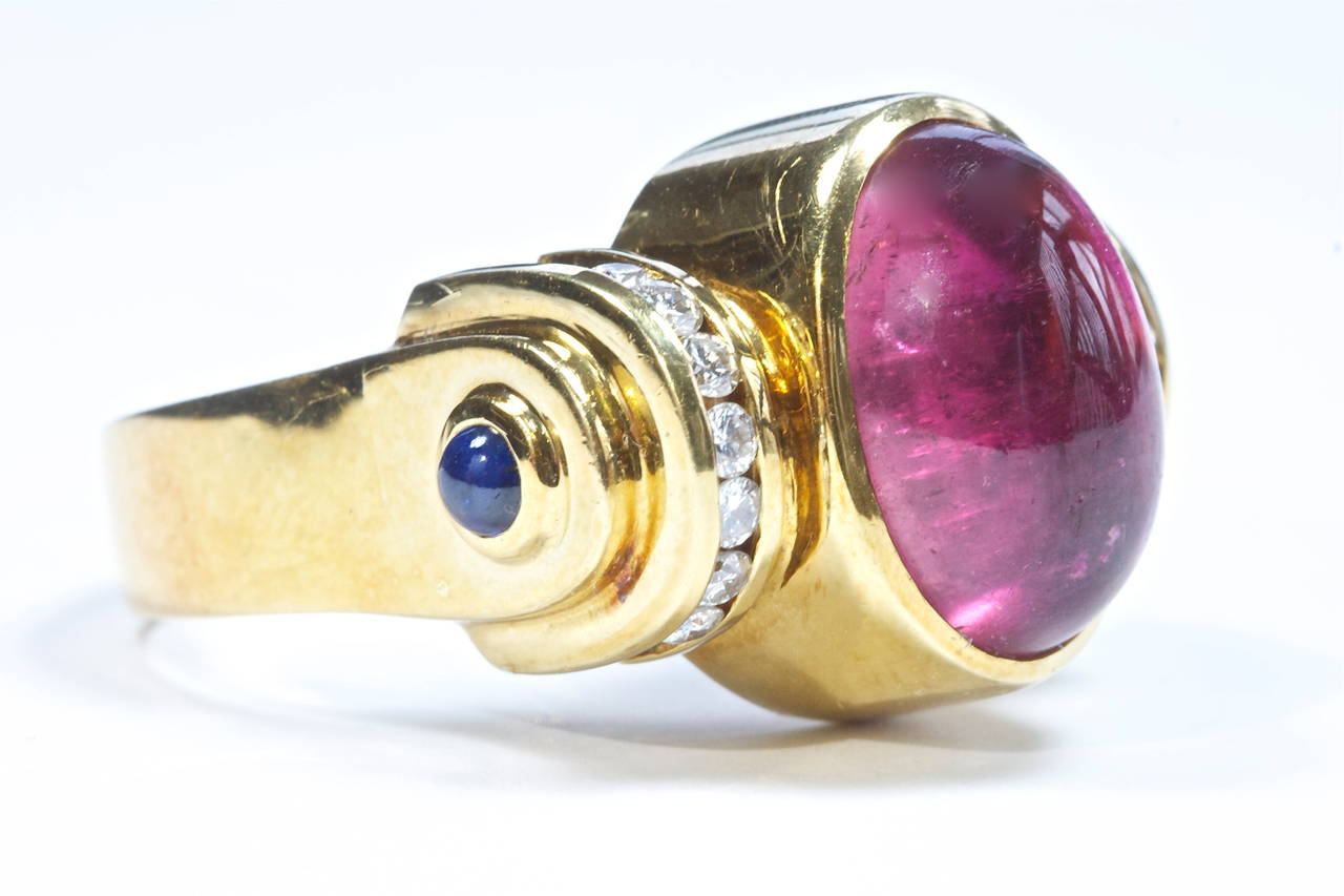 A color combination from the American jewelry designer Lagos. At the center is a deep pink cabochon tourmaline accented by channel set white diamonds set in 18k gold leading you down to two cabochon cut blue sapphires. 
Signed Lagos.

Size 9 and