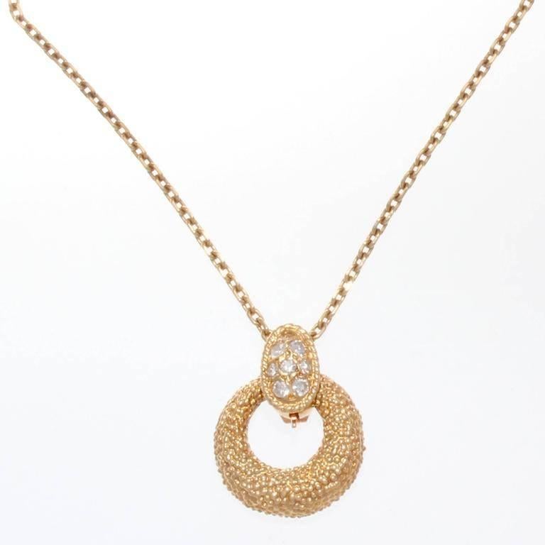 Van Cleef & Arpels, a long rich history of trend setting fashion that is still relevant today. The pendant is fashioned with near colorless diamonds that is gently grasping a doughnut of textured 18k yellow gold oval. Signed VCA and numbered. 